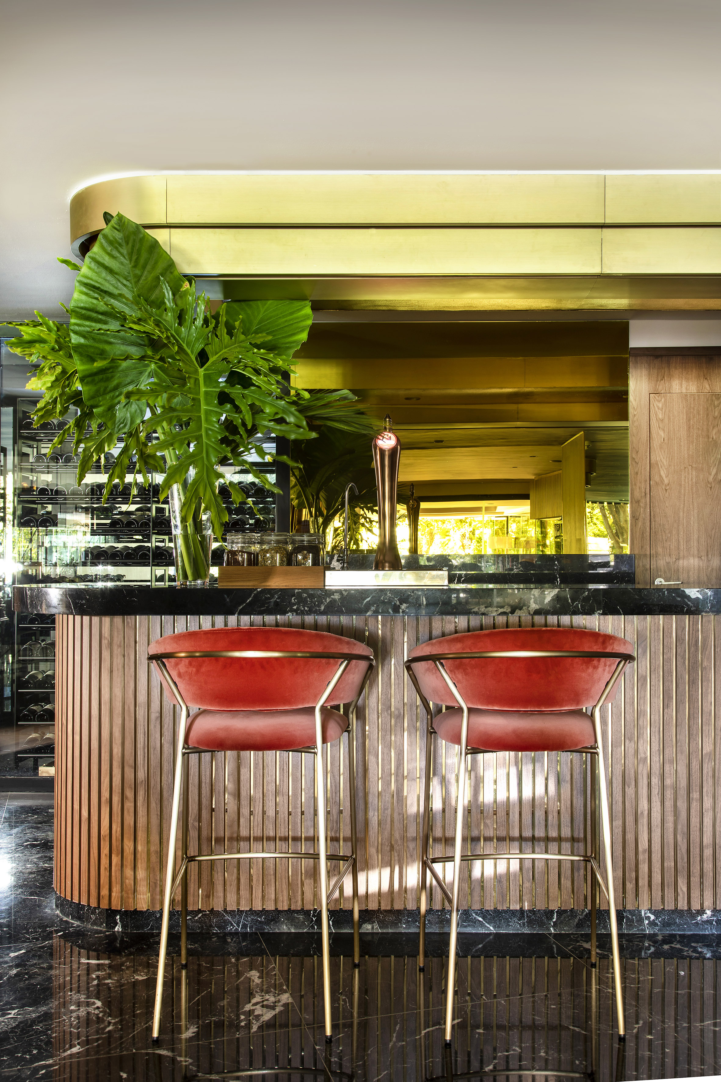 Contemporary bar with red velvet stools, marble counter, and wine cellar display.