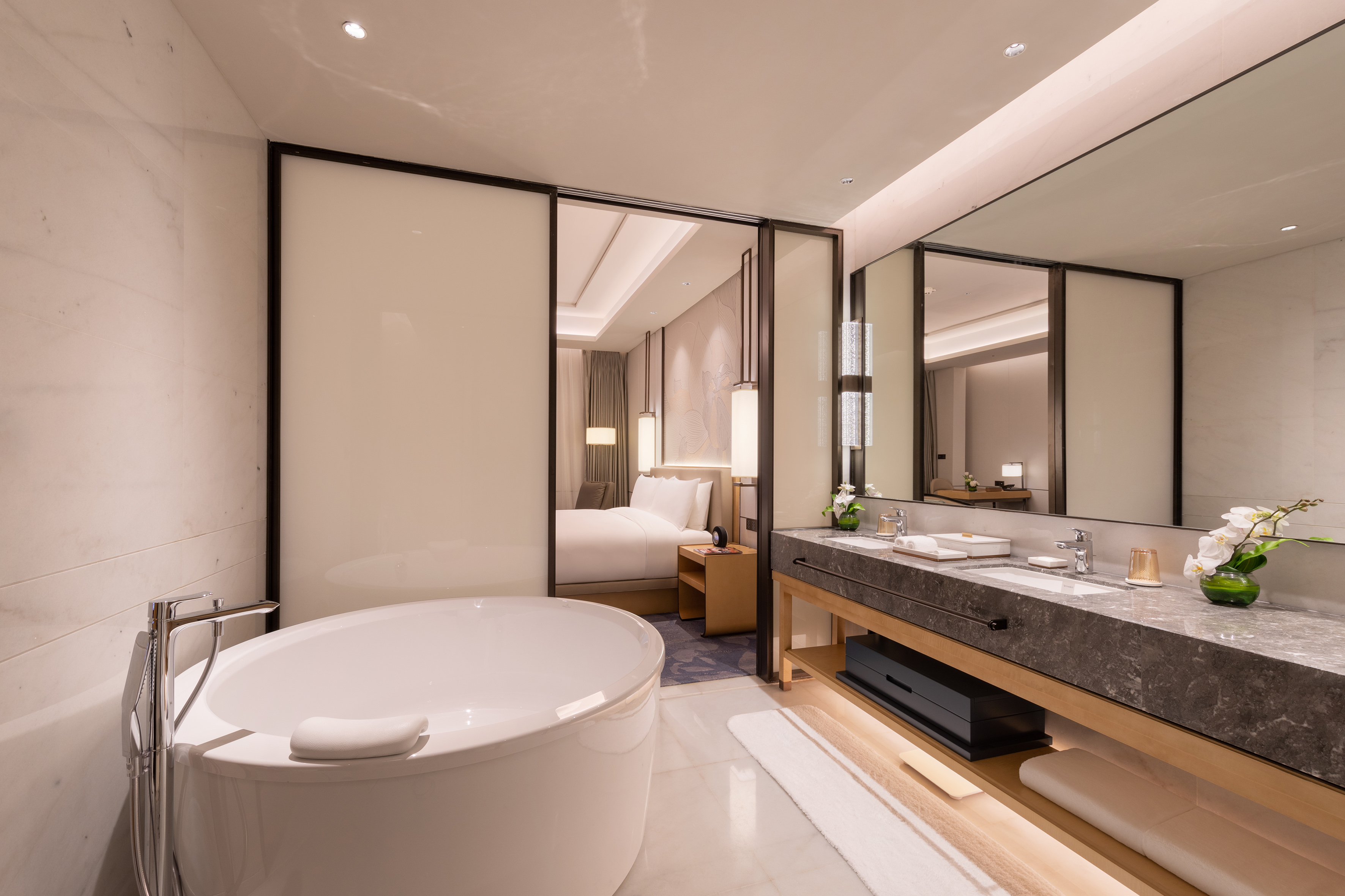 Luxury hotel bathroom with freestanding tub, double vanity, and bedroom view.