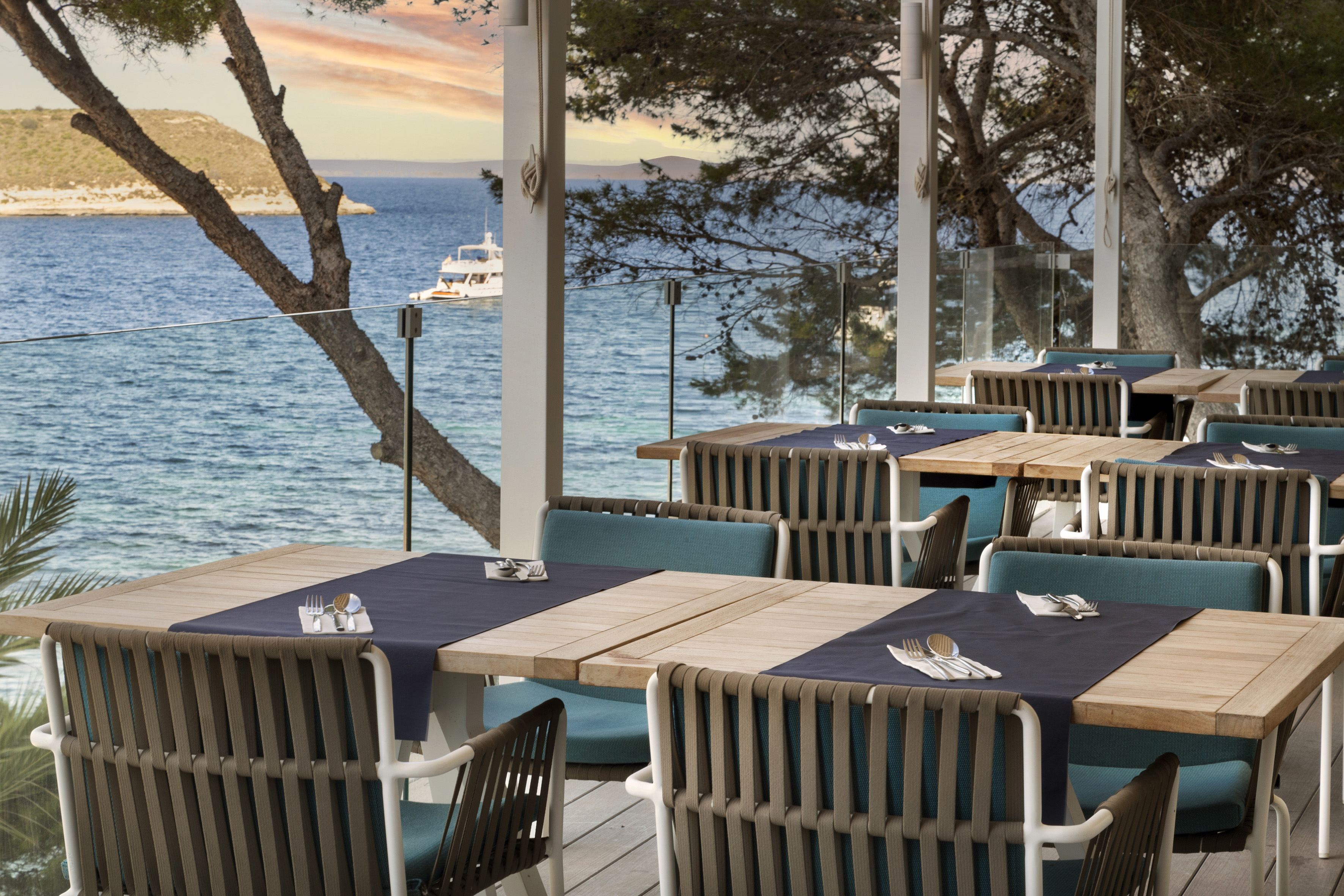 Seaside restaurant terrace with modern dining tables, ocean view, and a yacht.