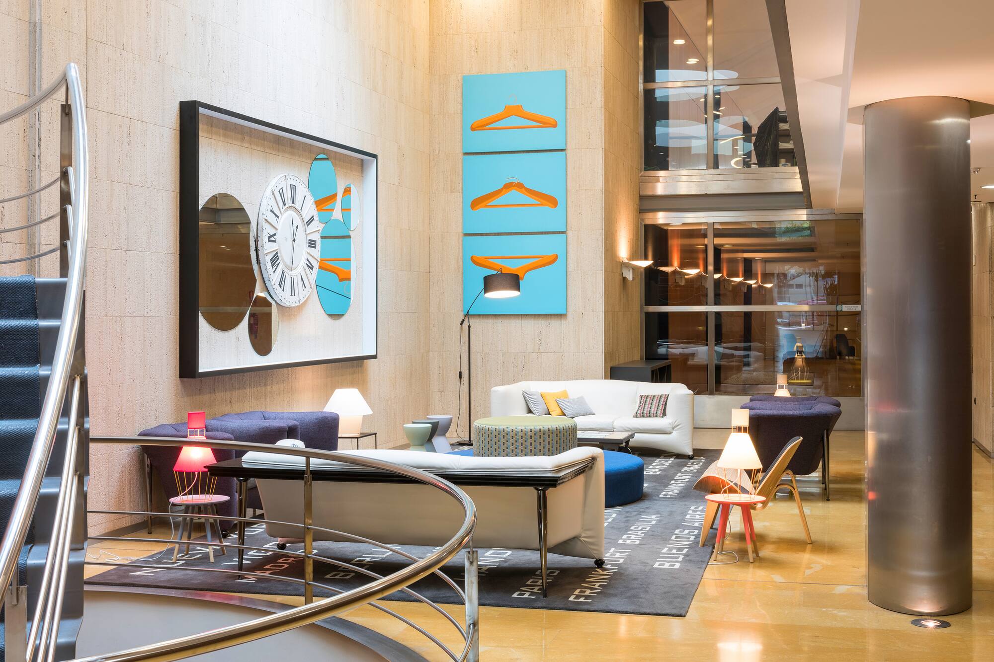 Modern hotel lobby lounge with spiral staircase, seating, city rug, and wall art.