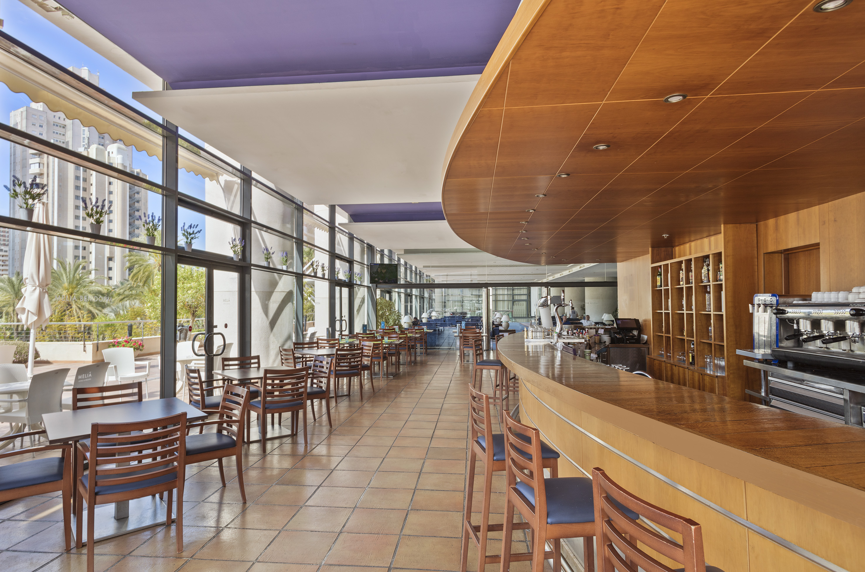 Modern hotel bar and restaurant with wood counter, tables, and city views.