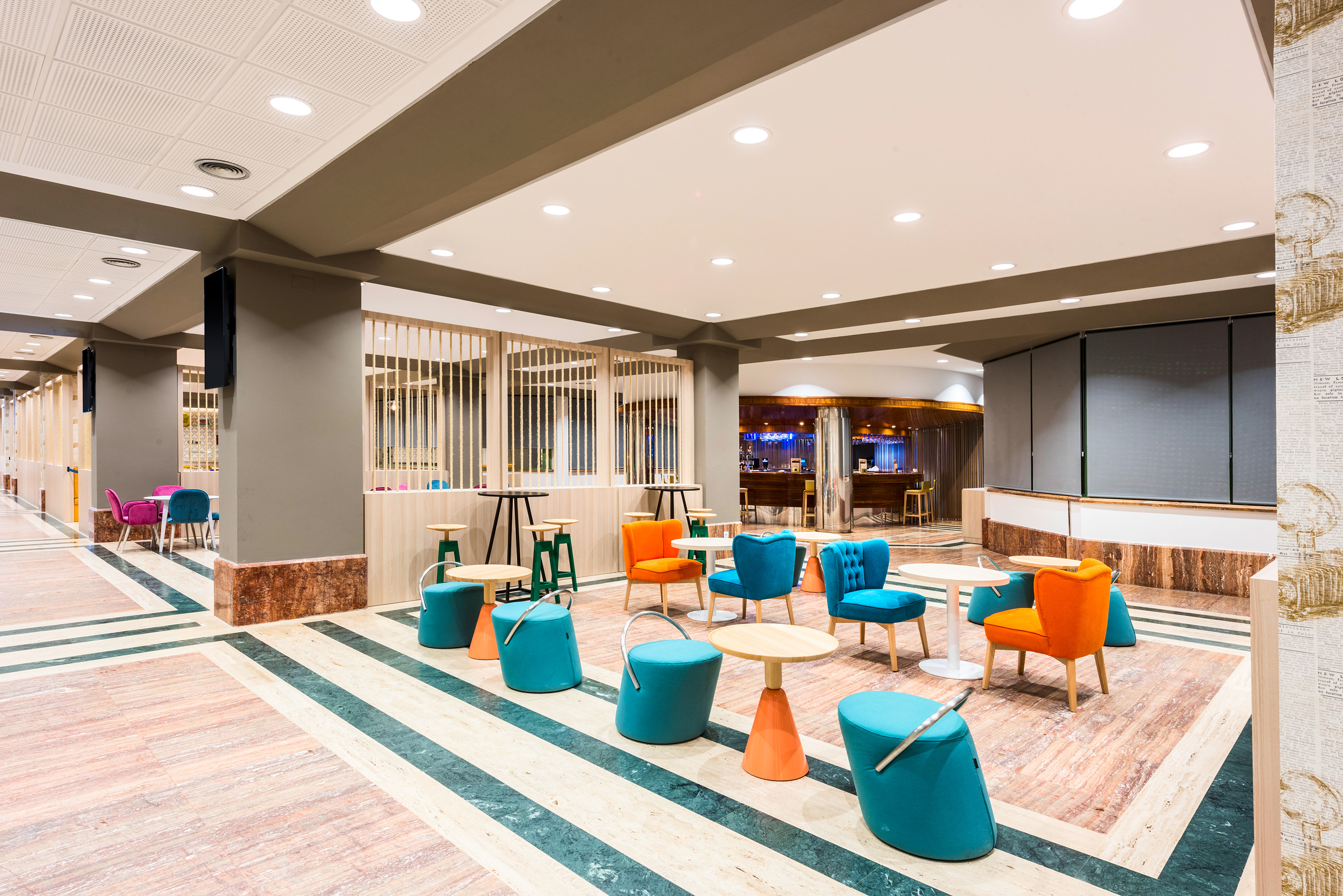 Modern hotel lobby with colorful seating, patterned marble floor, and bar area.