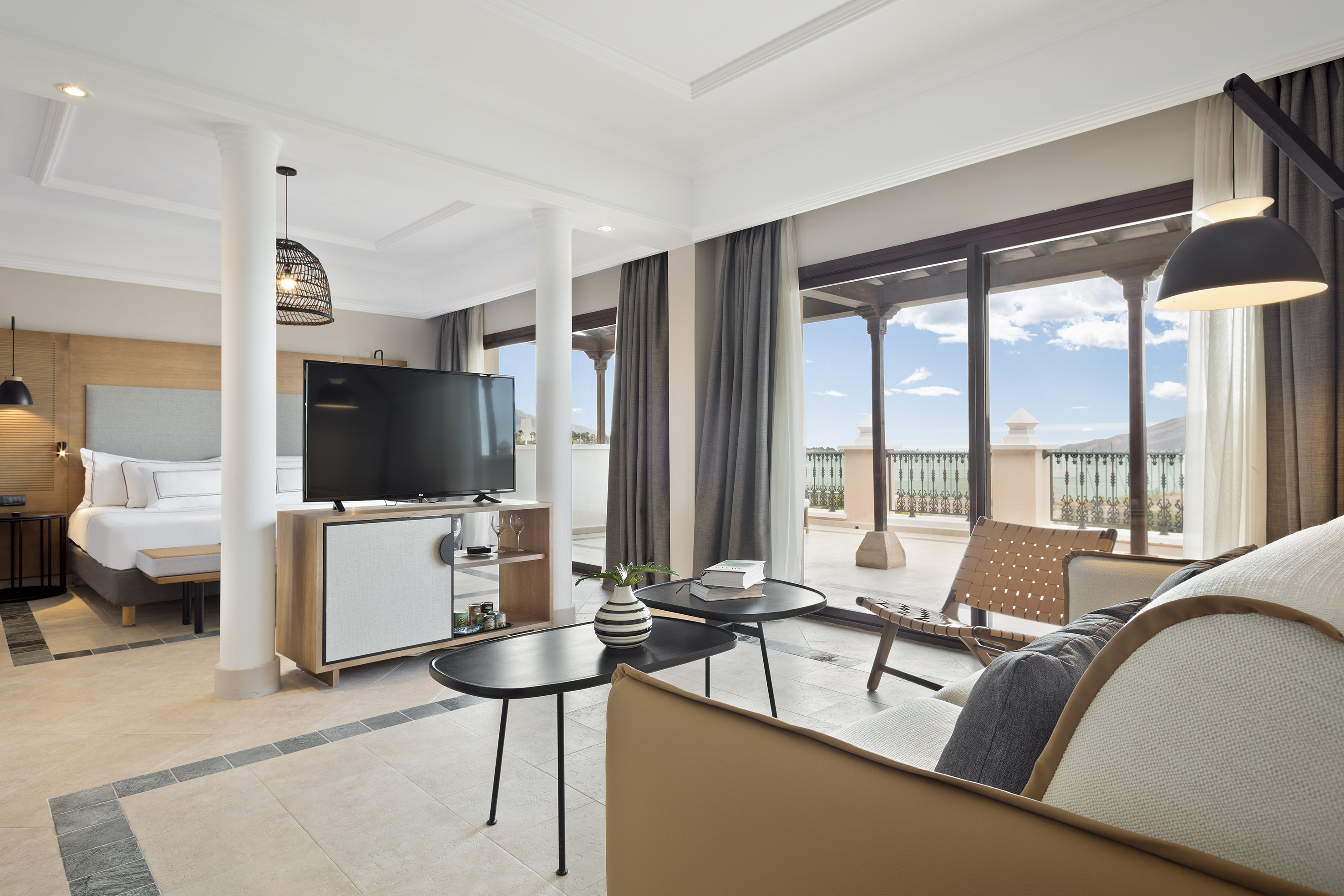 Modern hotel suite featuring king bed, living space, and balcony with scenic views.