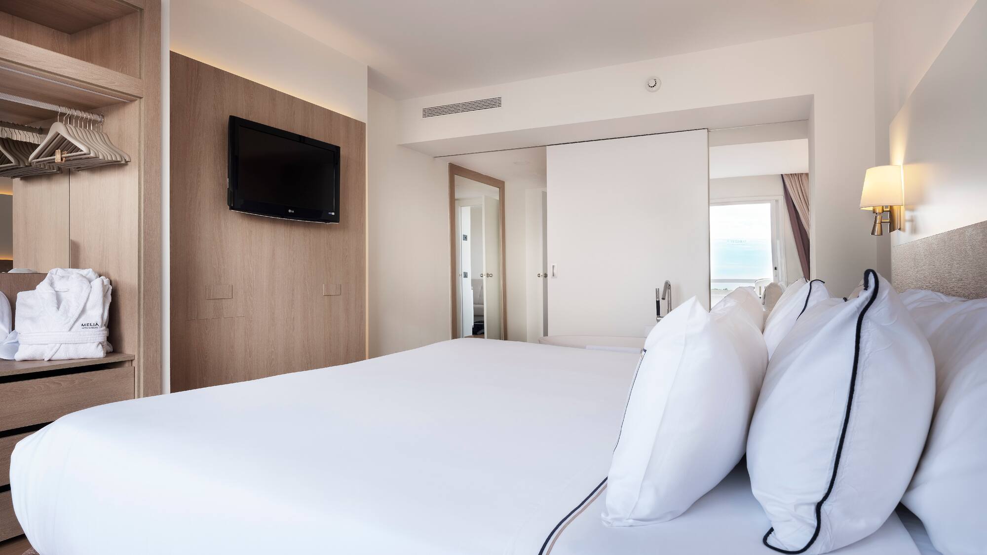 a bed with white sheets and a television on the wall