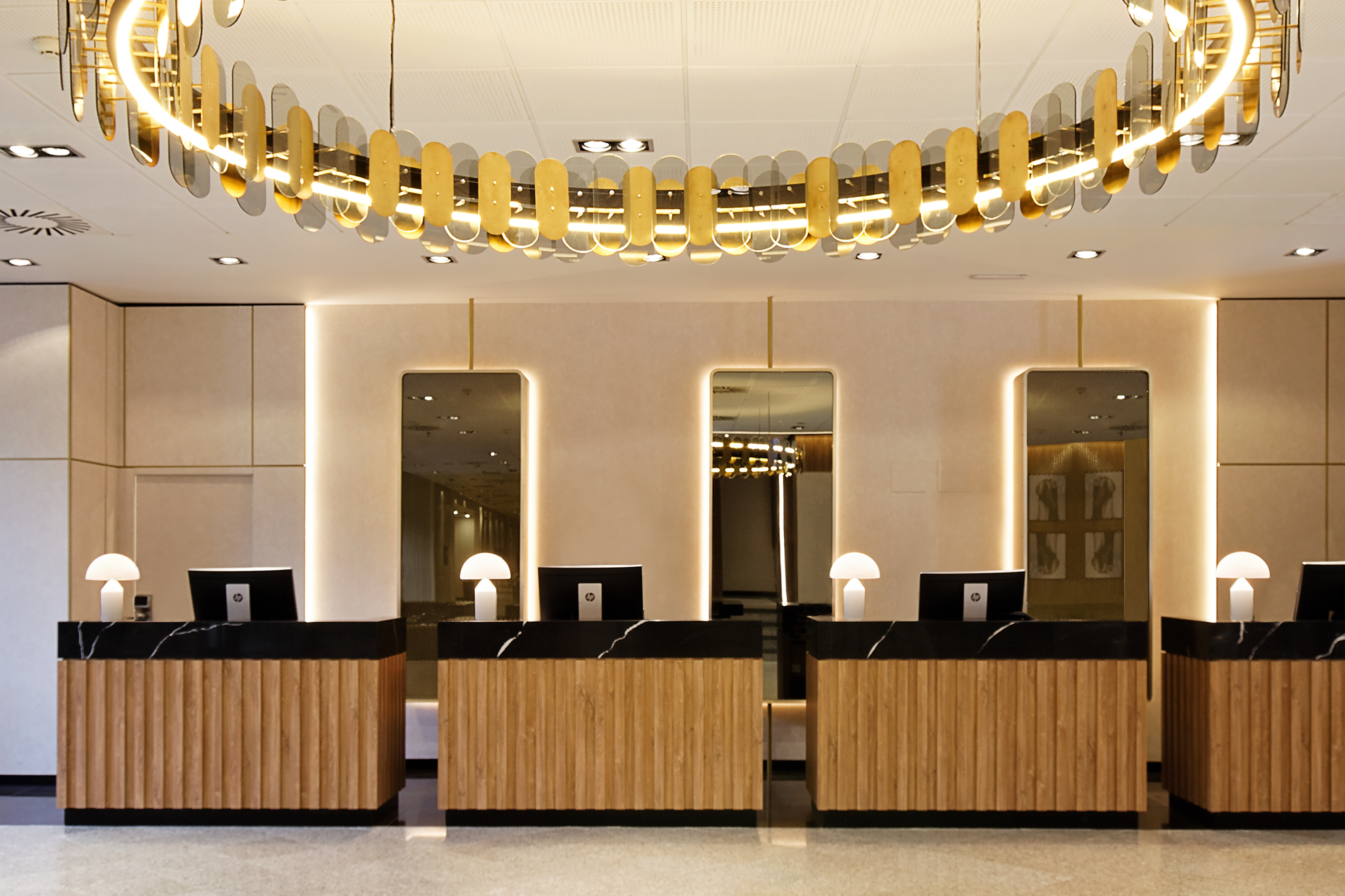 Modern hotel reception with wood and marble desks and a striking gold chandelier.
