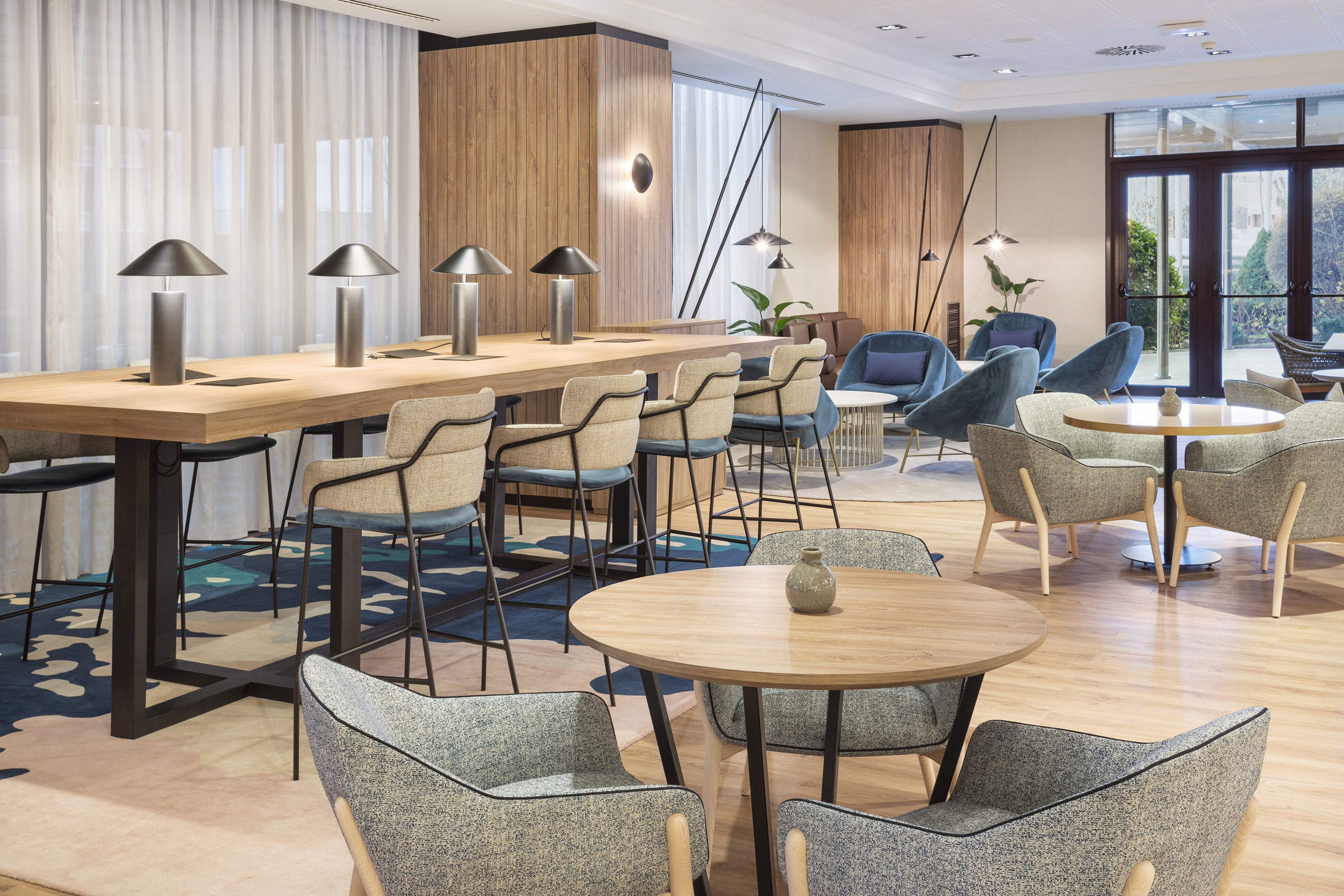 Modern hotel lobby with communal work table, bar stools, and lounge seating.