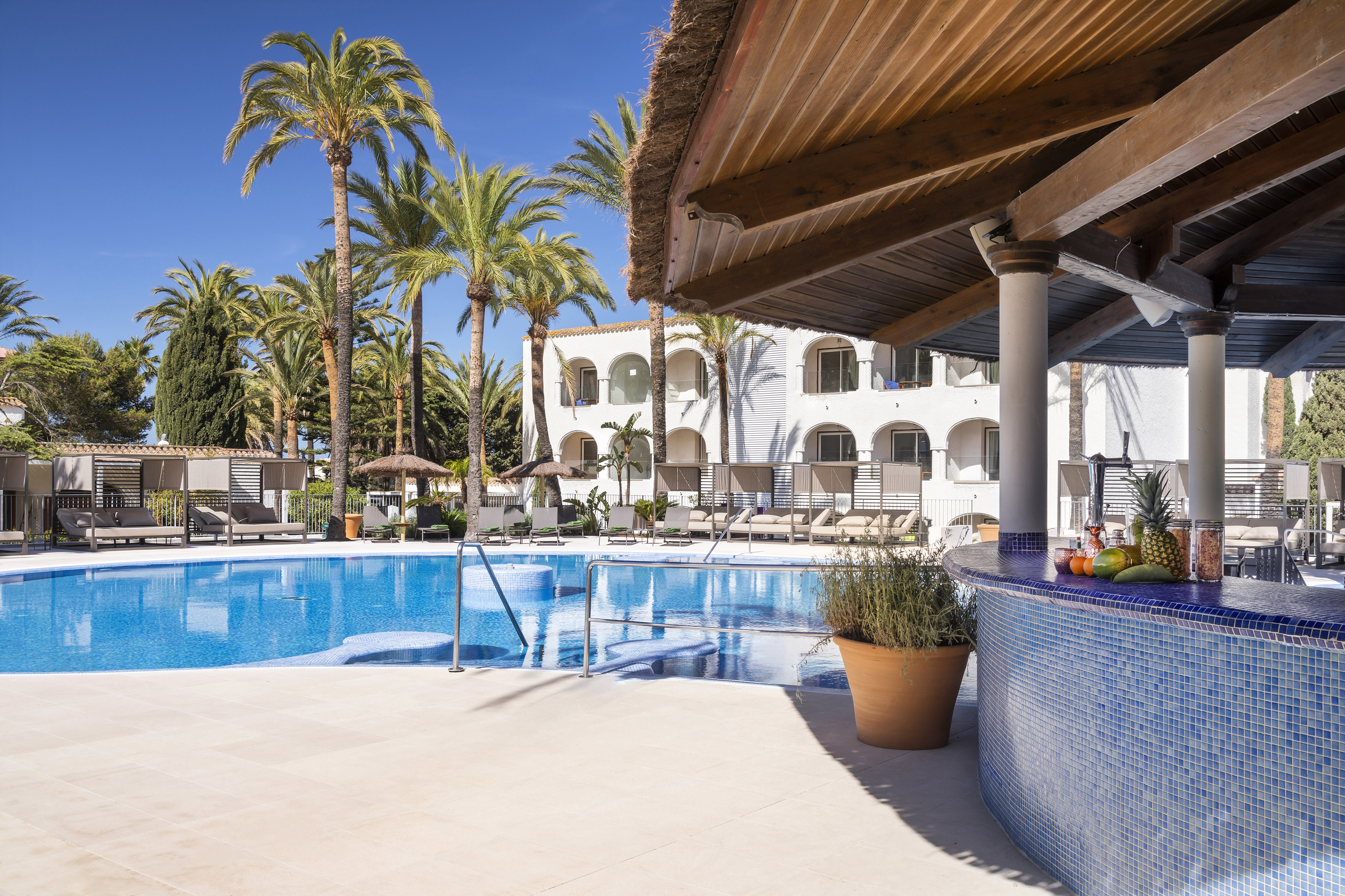 Sunny resort pool with blue mosaic poolside bar and palm trees.