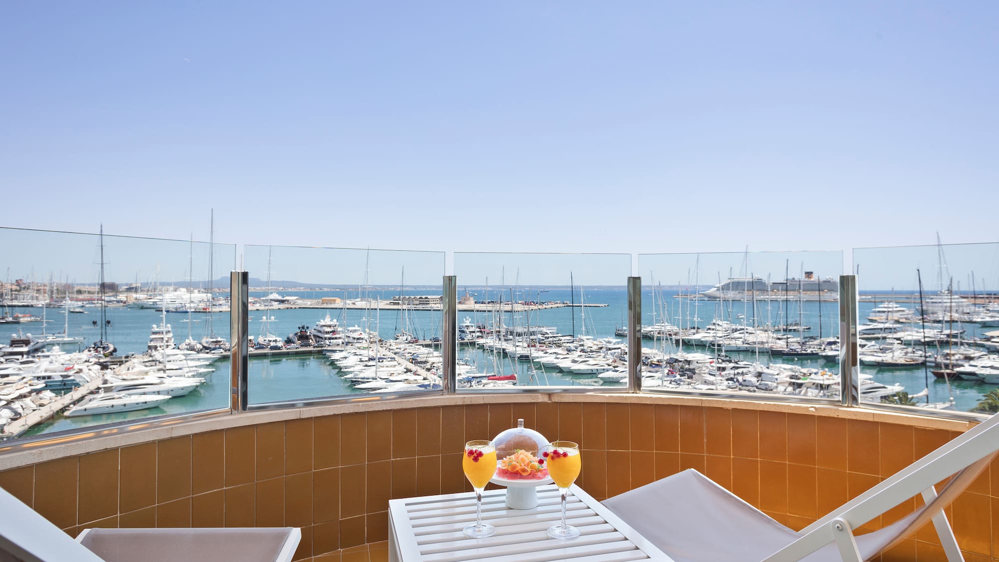 a table with drinks and chairs on a balcony overlooking a body of water