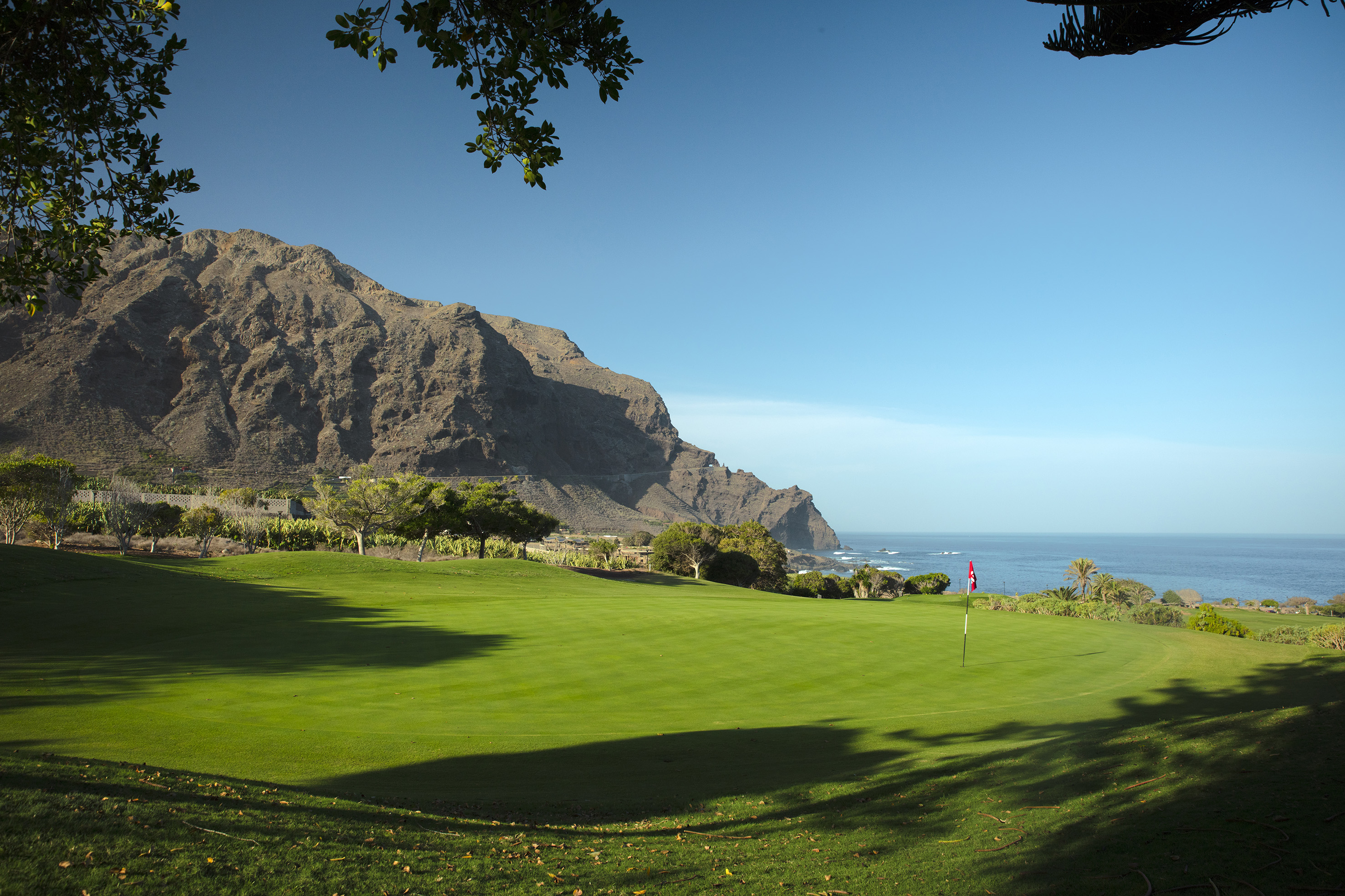 Seaside golf course with green, flag, mountain, and ocean view.
