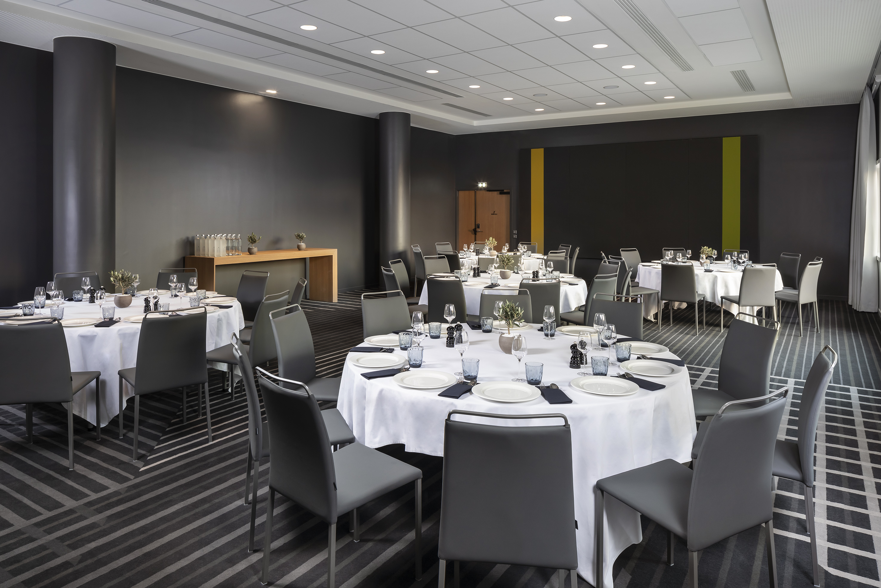 Modern conference room with round tables, white linens, and grey chairs.
