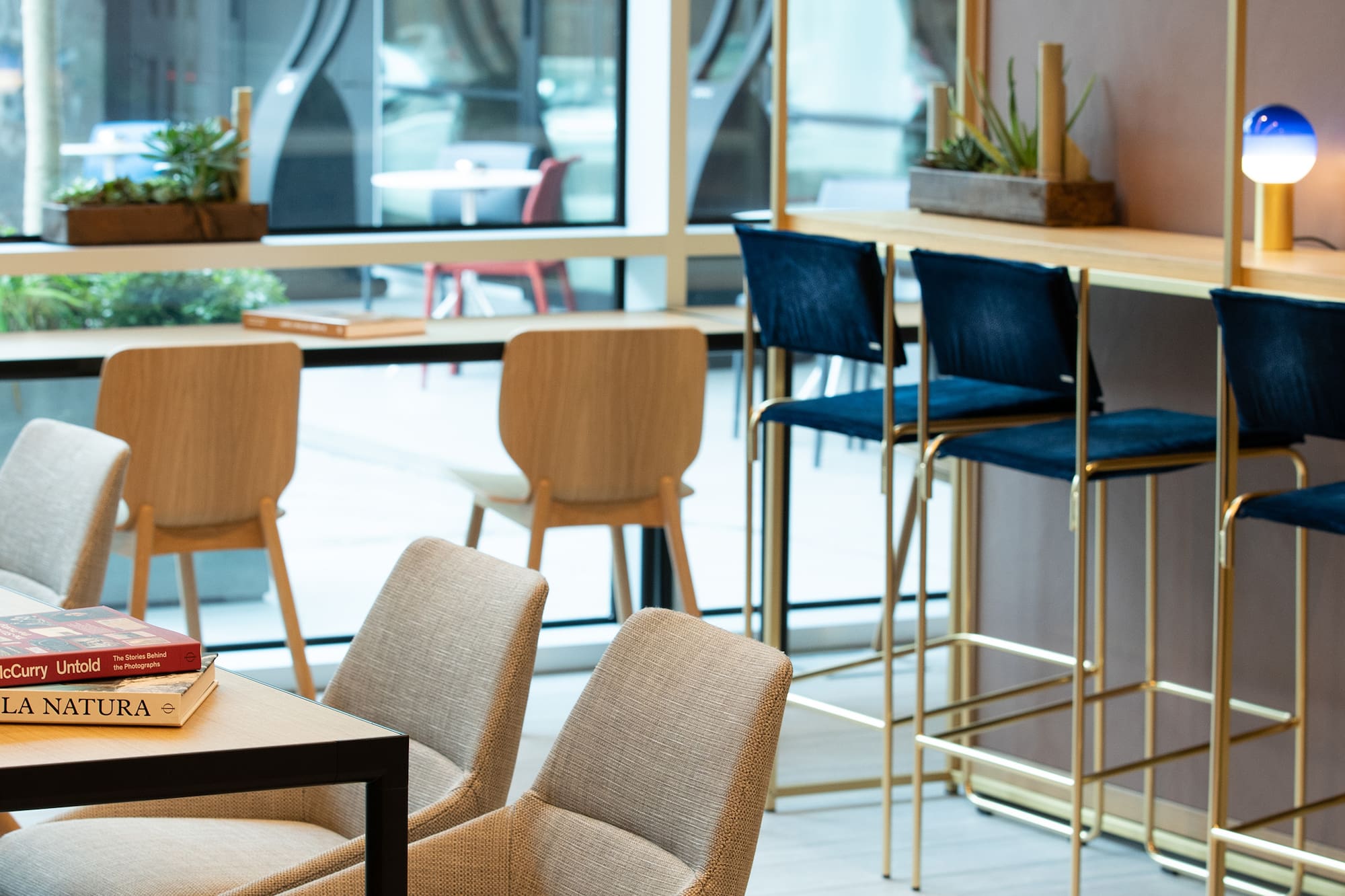Modern lounge with diverse seating, bar stools, plants, and large windows.