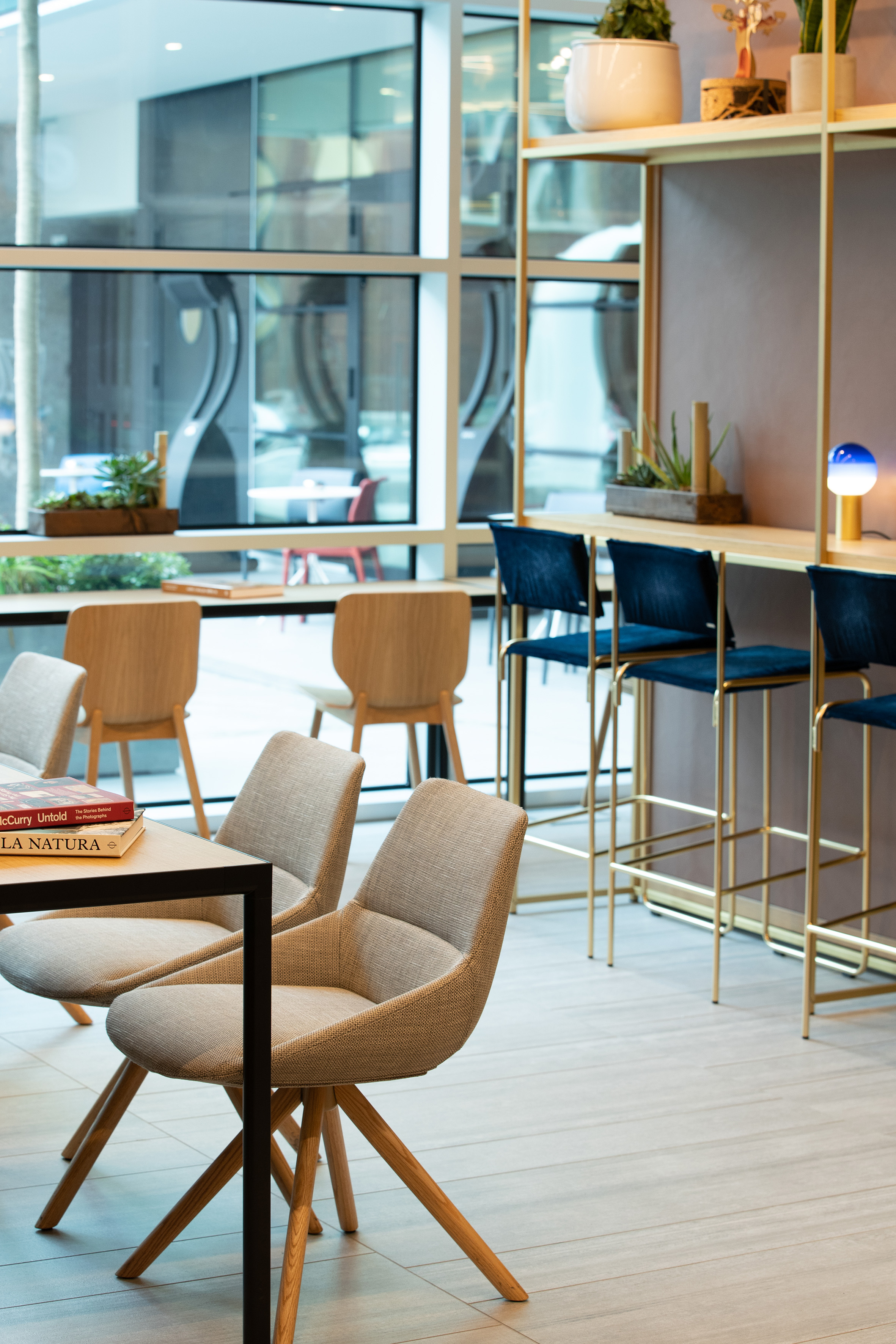 Modern lounge with diverse seating, bar stools, plants, and large windows.