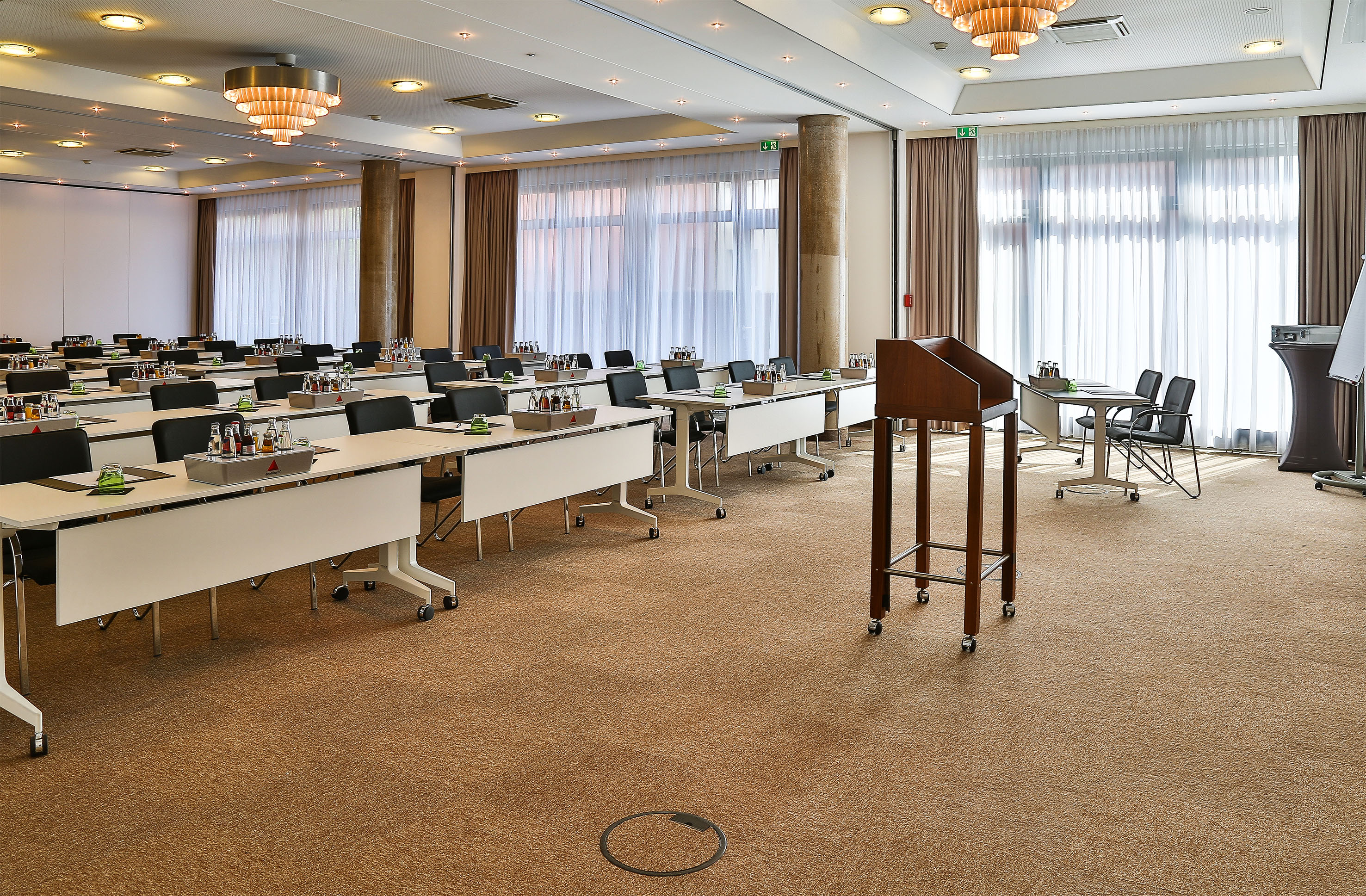 Set up conference room with rows of tables, chairs, drinks, and a wooden lectern.