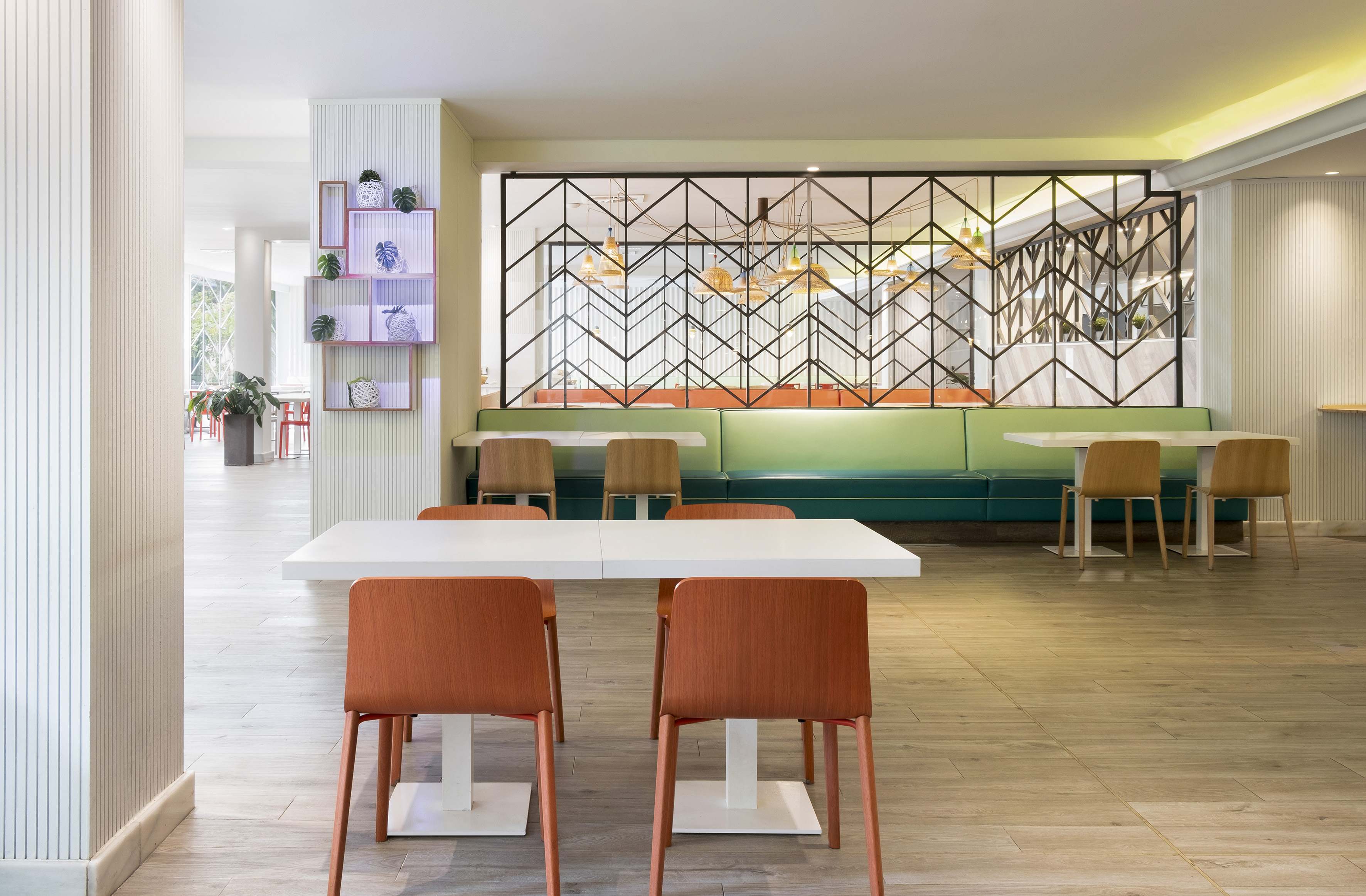 Modern dining area with white tables, wood chairs, green banquette, geometric screen.