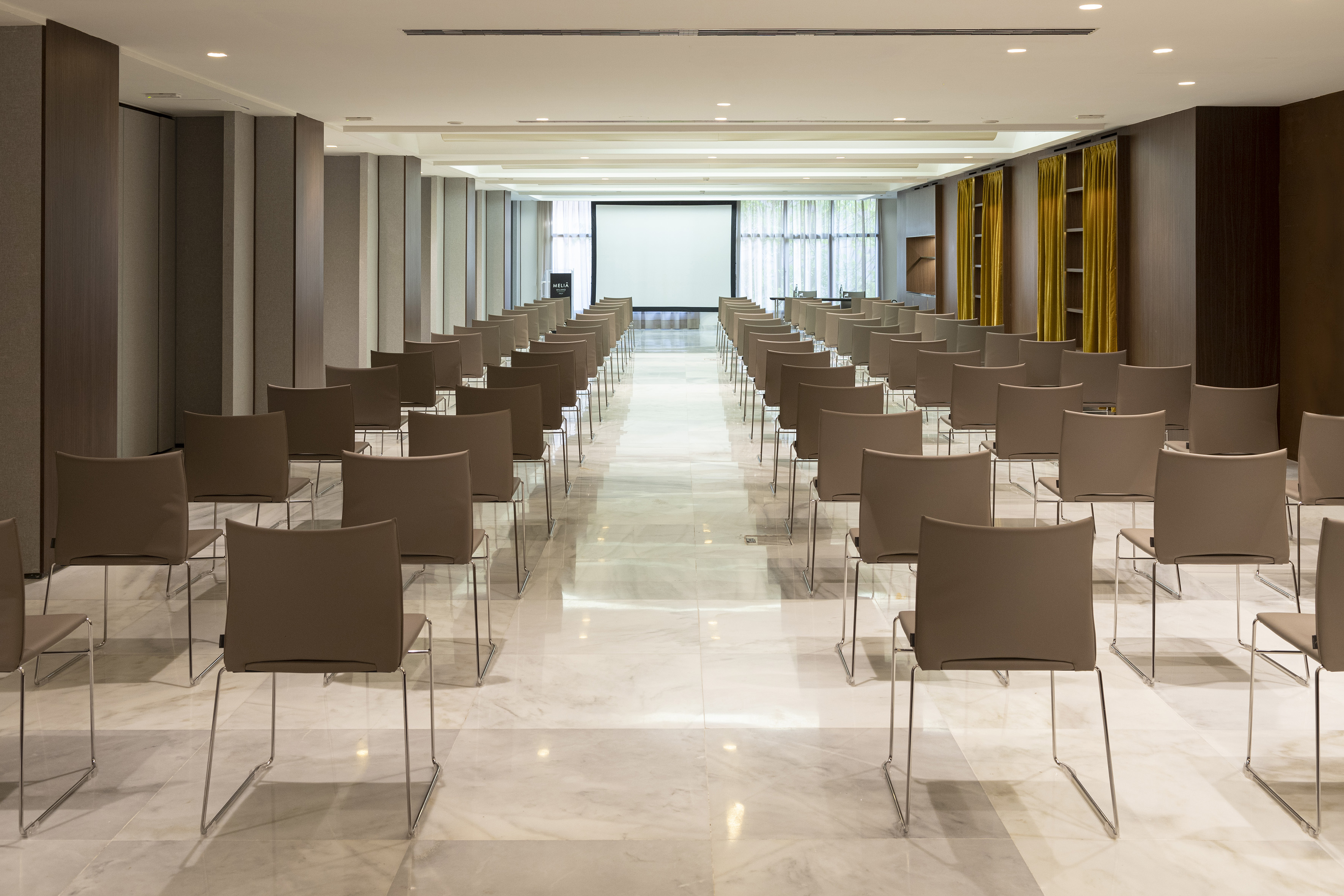 Modern conference room with rows of chairs, large screen, and marble floor.