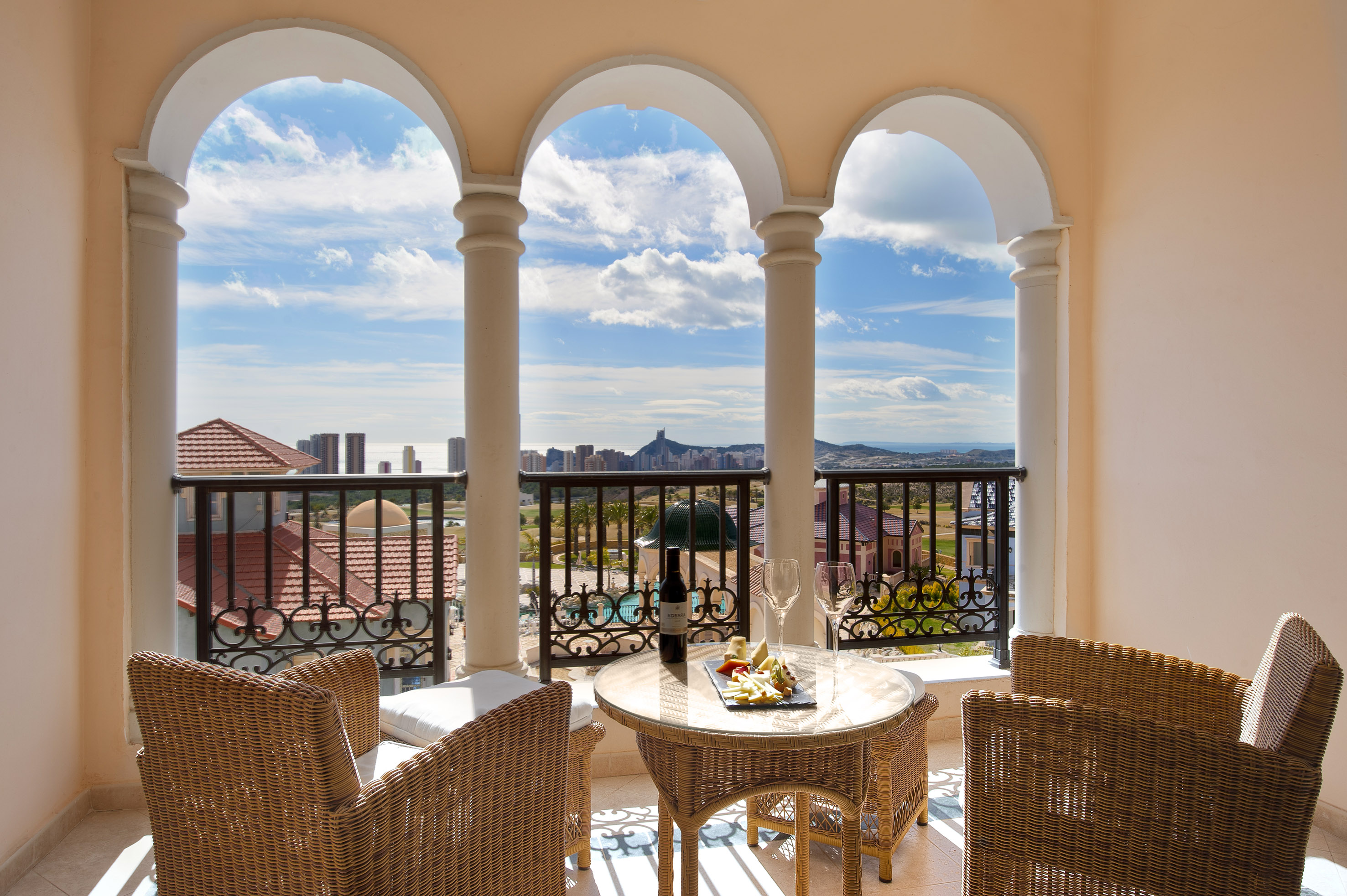 Arched balcony with ocean & city views, wicker chairs, wine and cheese table.