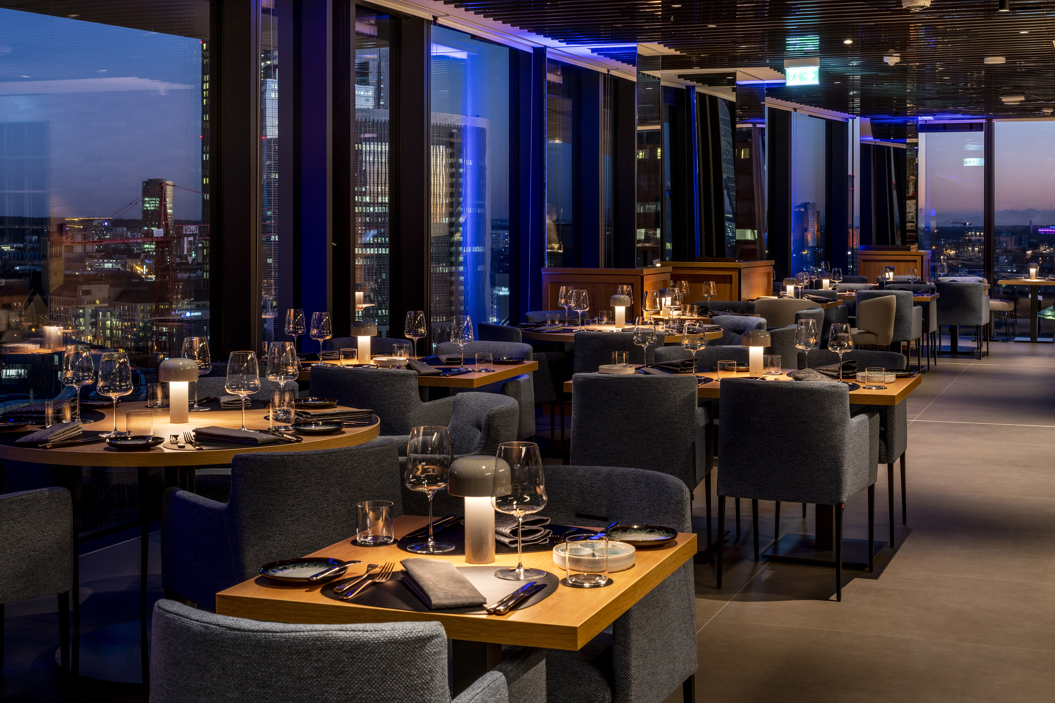 Elegant restaurant with night city view, modern tables, and gray chairs.