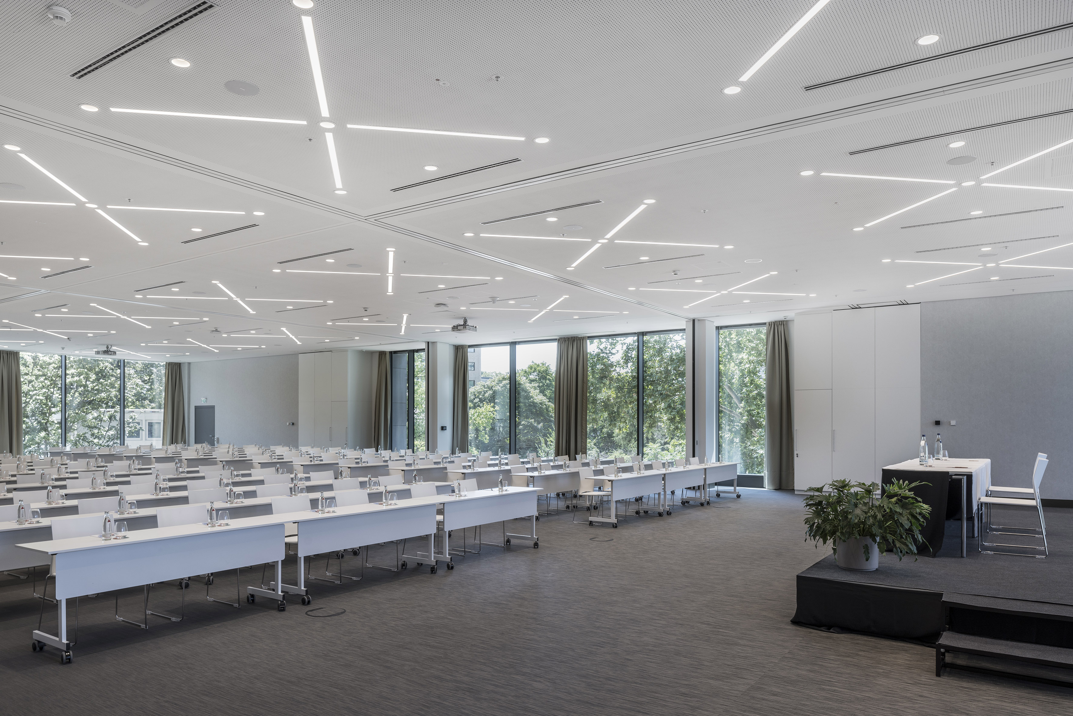 Modern conference room with rows of tables, natural light, and stage area.
