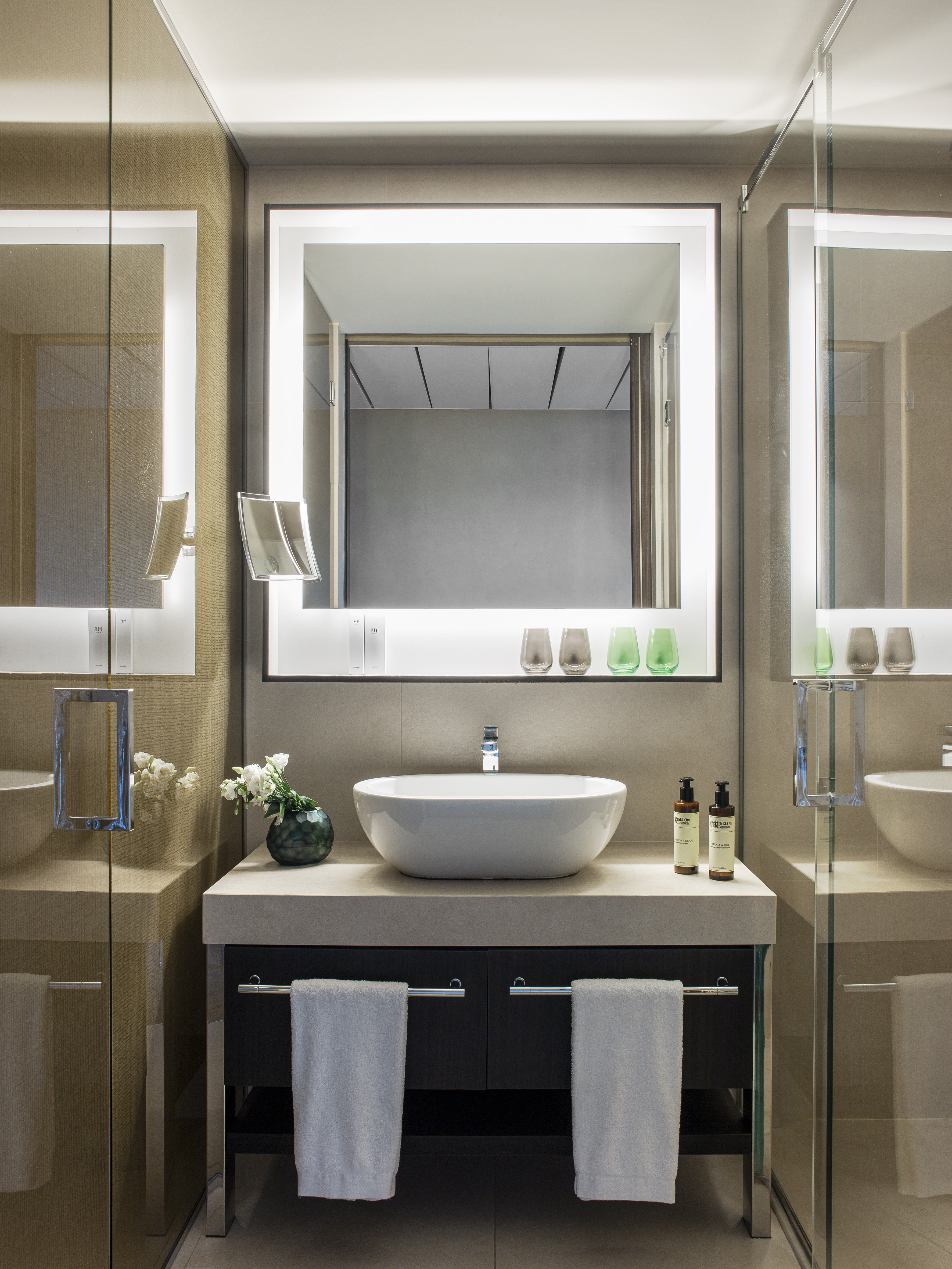 Modern bathroom vanity with white vessel sink, lighted mirror, and glass shower.