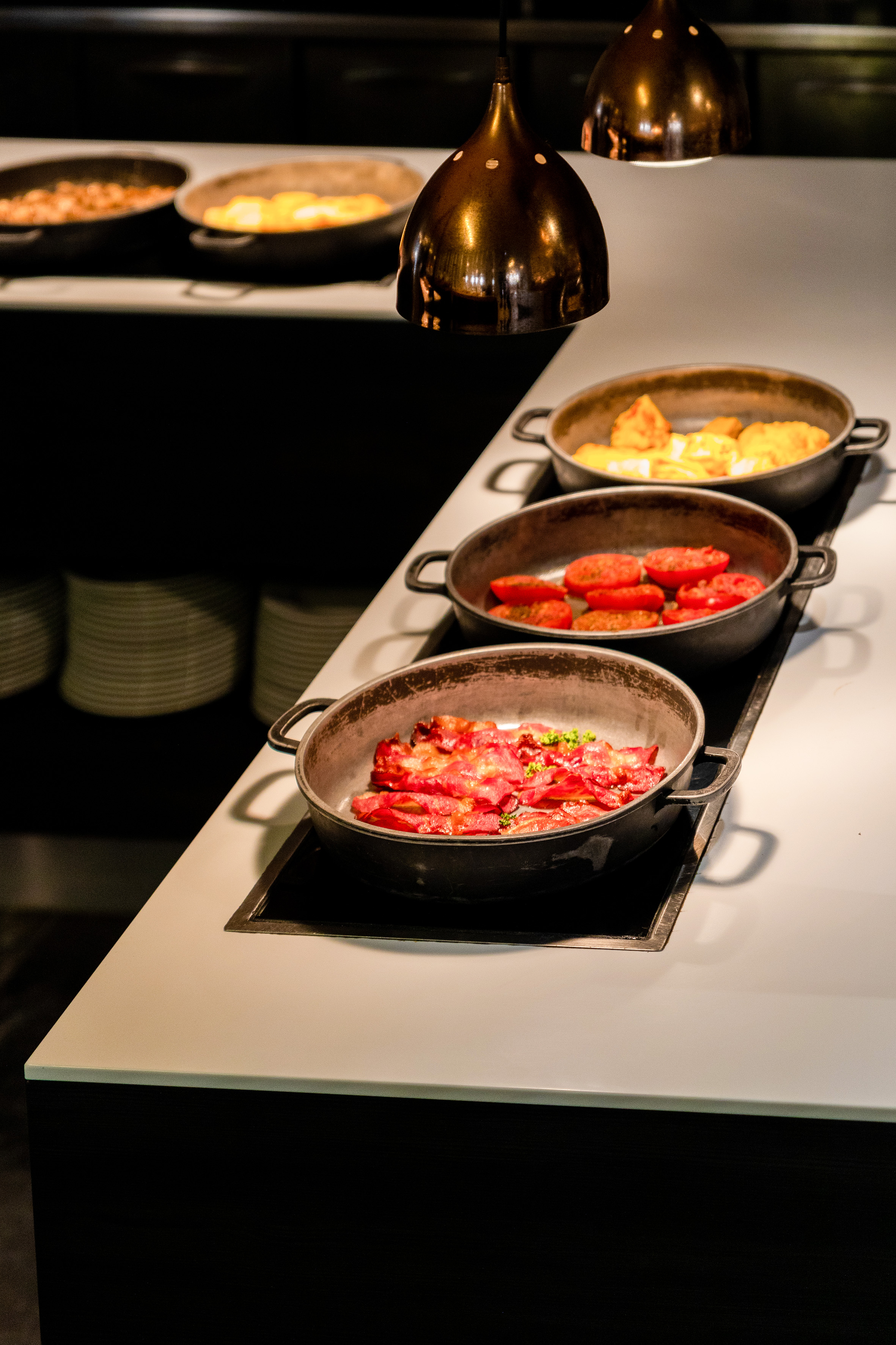 Hot breakfast buffet with bacon, roasted tomatoes, and eggs in serving pans.