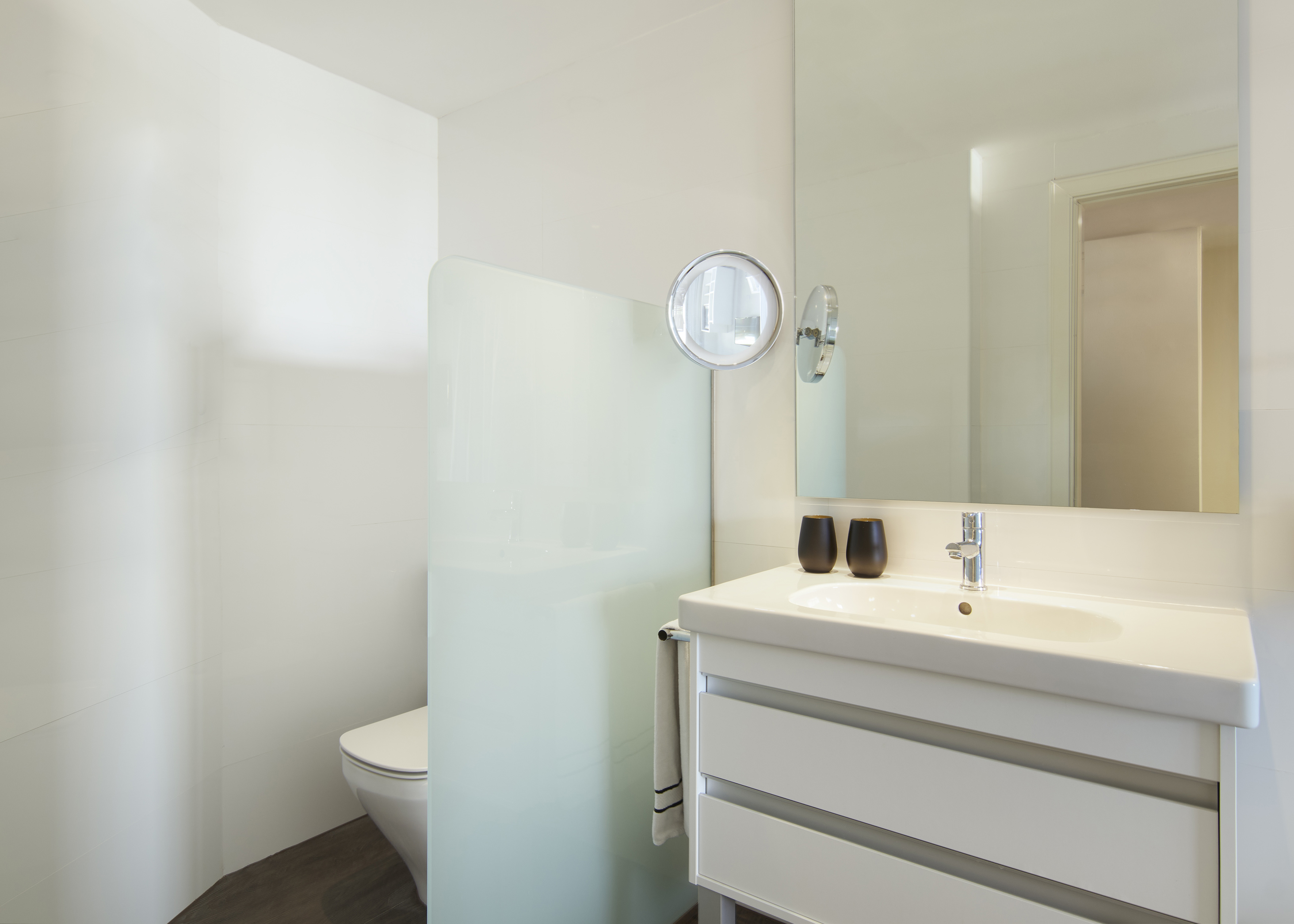 Modern white bathroom with vanity, sink, toilet, mirror, and glass divider.