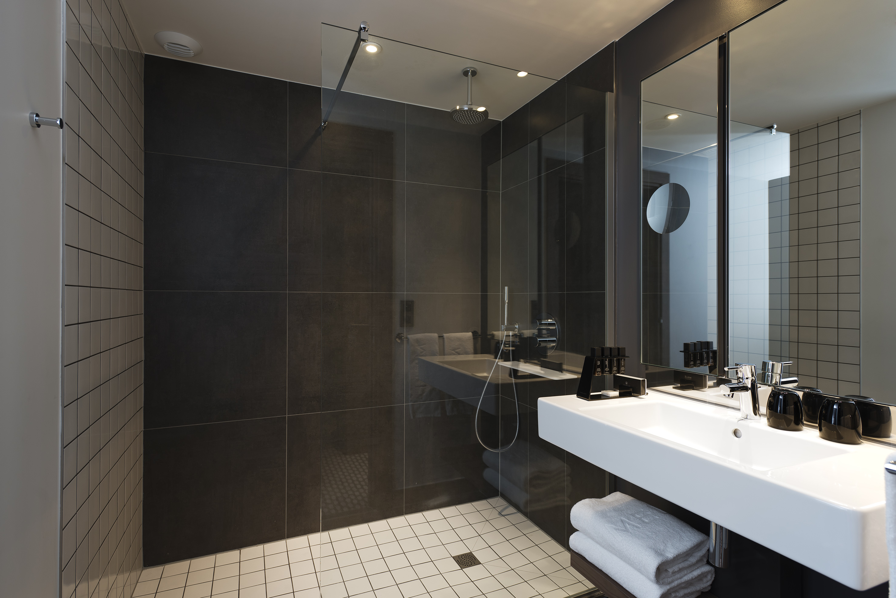 Contemporary bathroom featuring dark tiles, glass shower, and sleek white sink.