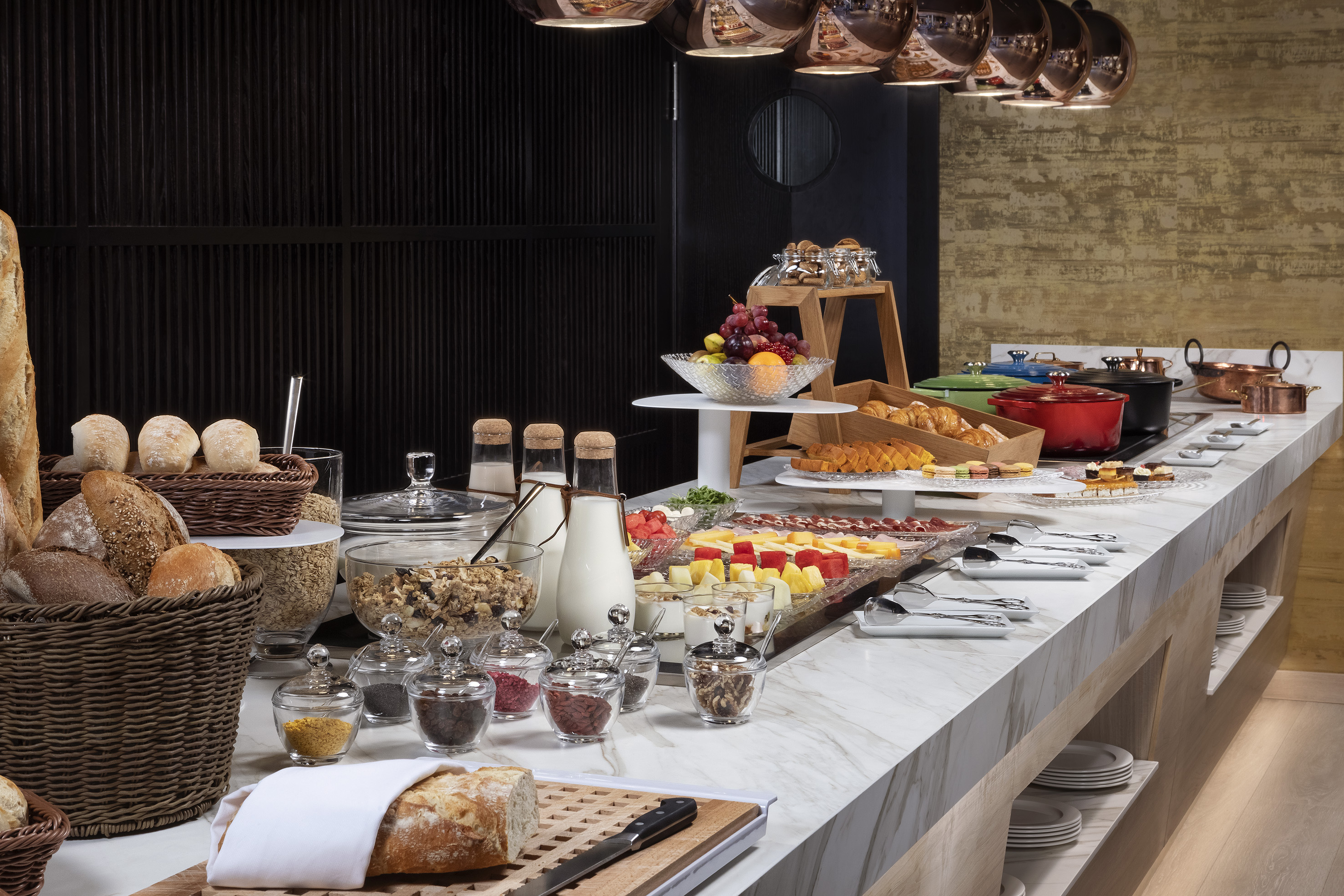Diverse breakfast buffet with bread, cheese, fruits, cereals, and hot dishes.