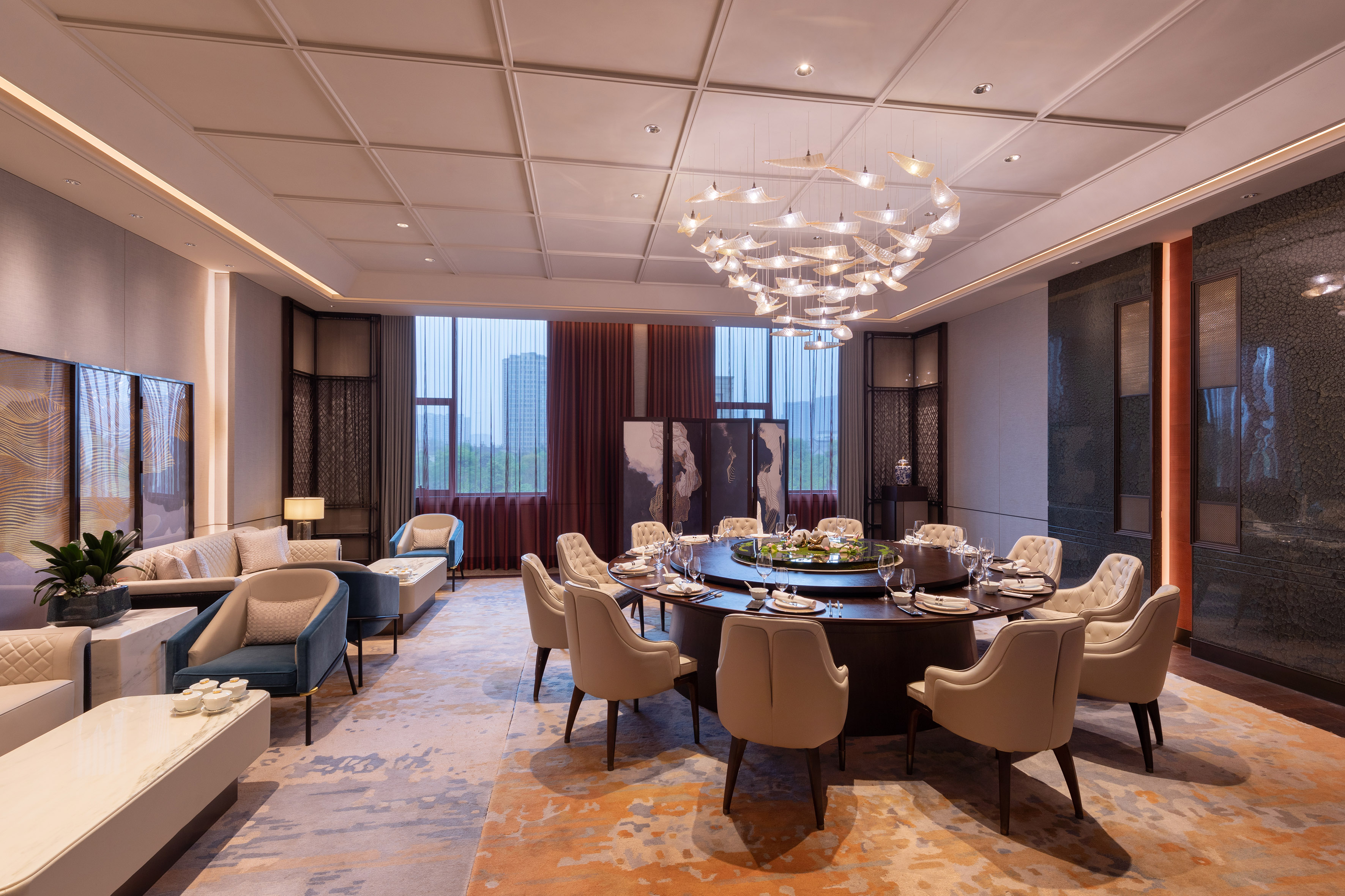 Modern luxury dining room with round table, elegant chandelier, and lounge seating.