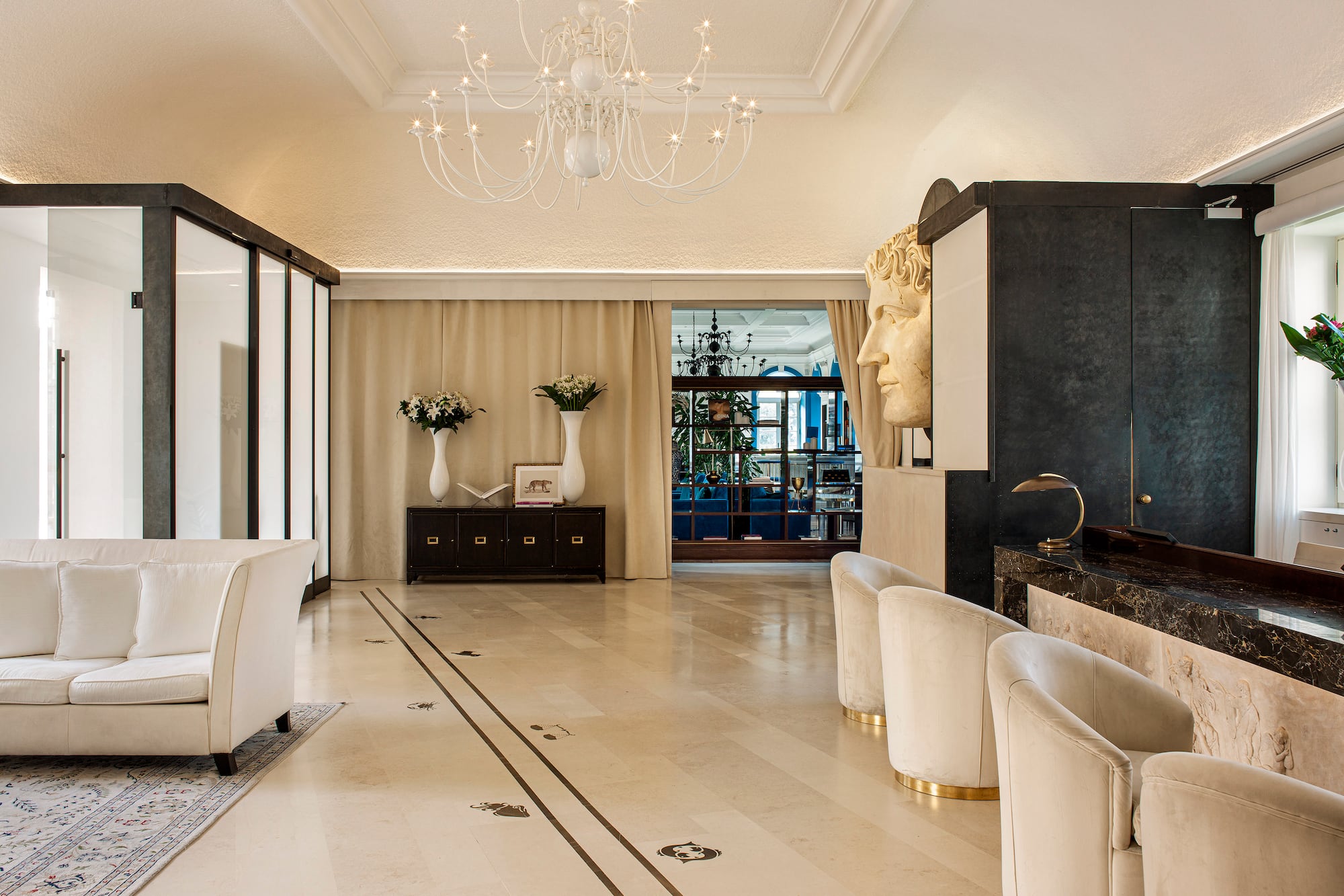 Luxury hotel lobby with marble floor, classical bust, white sofa, and chandelier.