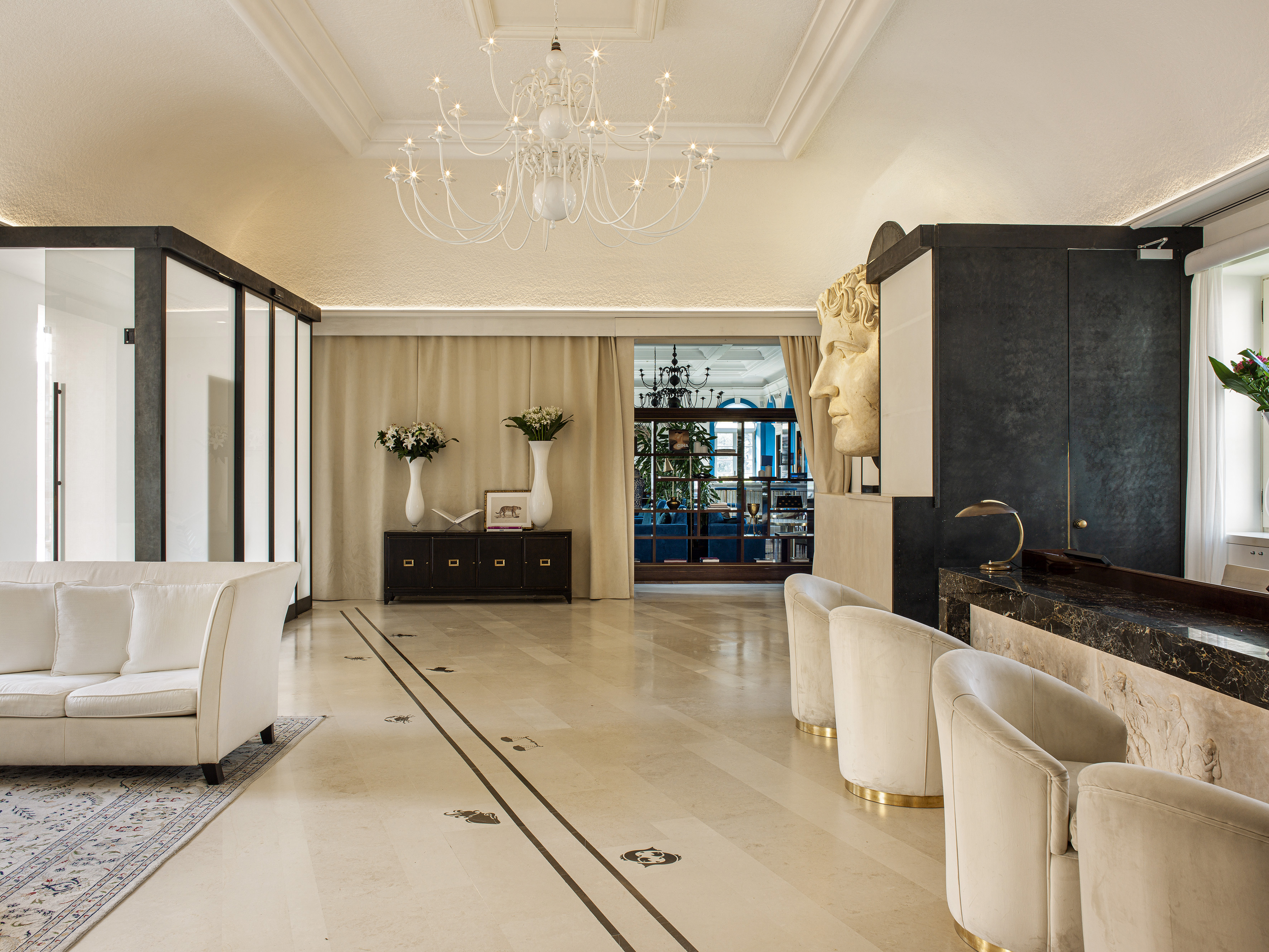 Luxury hotel lobby with marble floor, classical bust, white sofa, and chandelier.