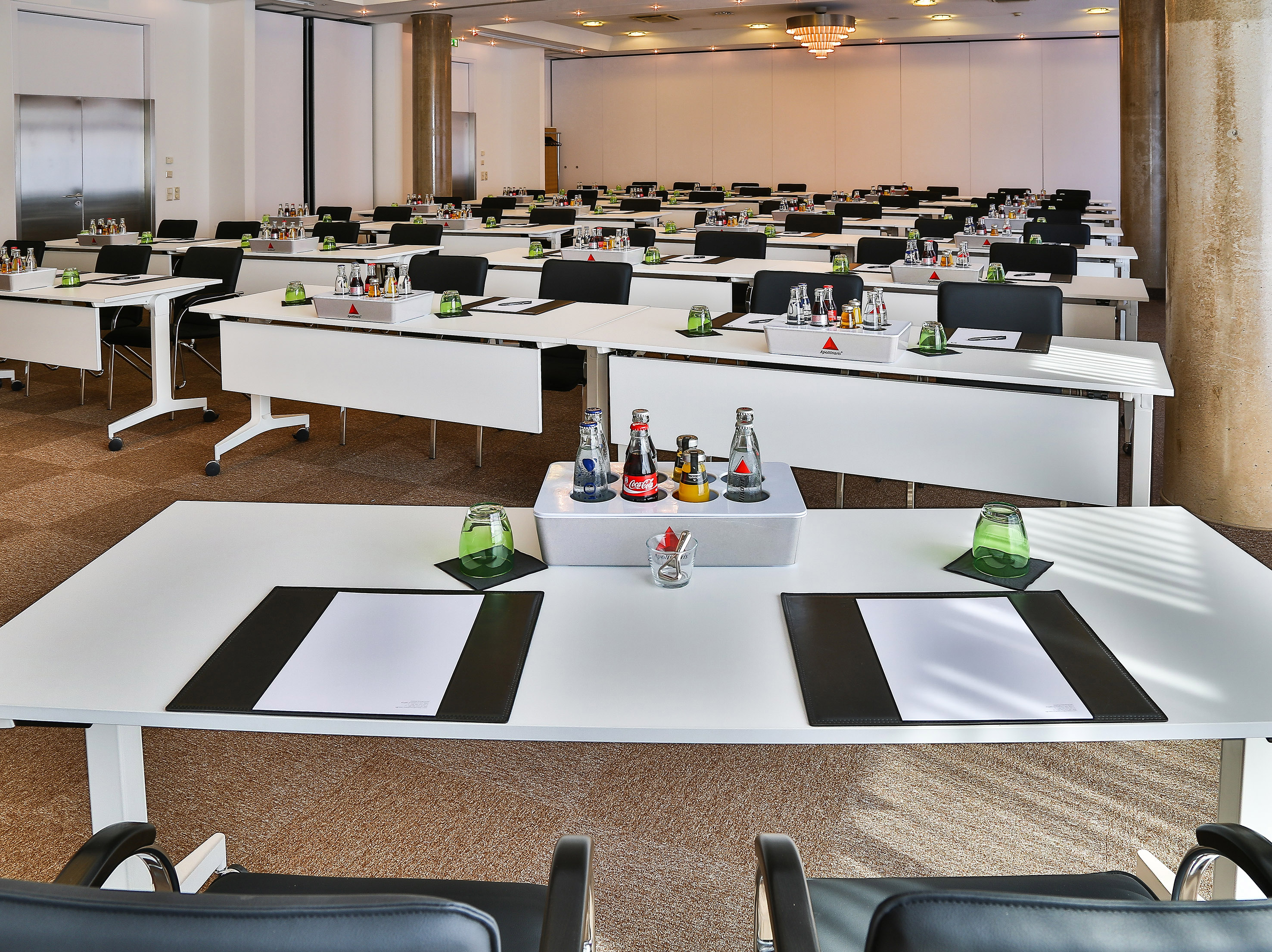 Professional conference room setup with white tables, chairs, and bottled drinks.