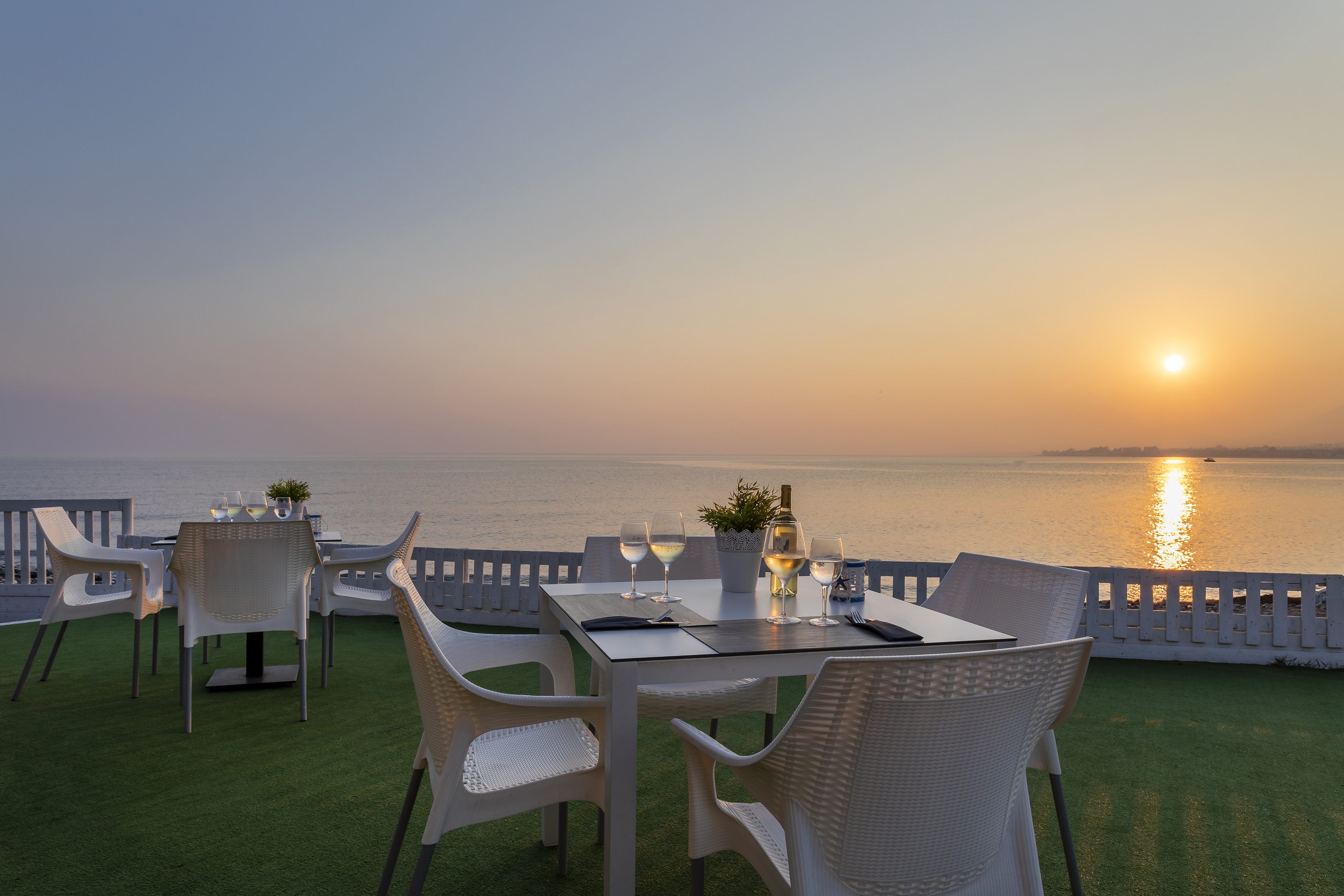 Outdoor dining terrace with ocean view at sunset, tables set with wine.