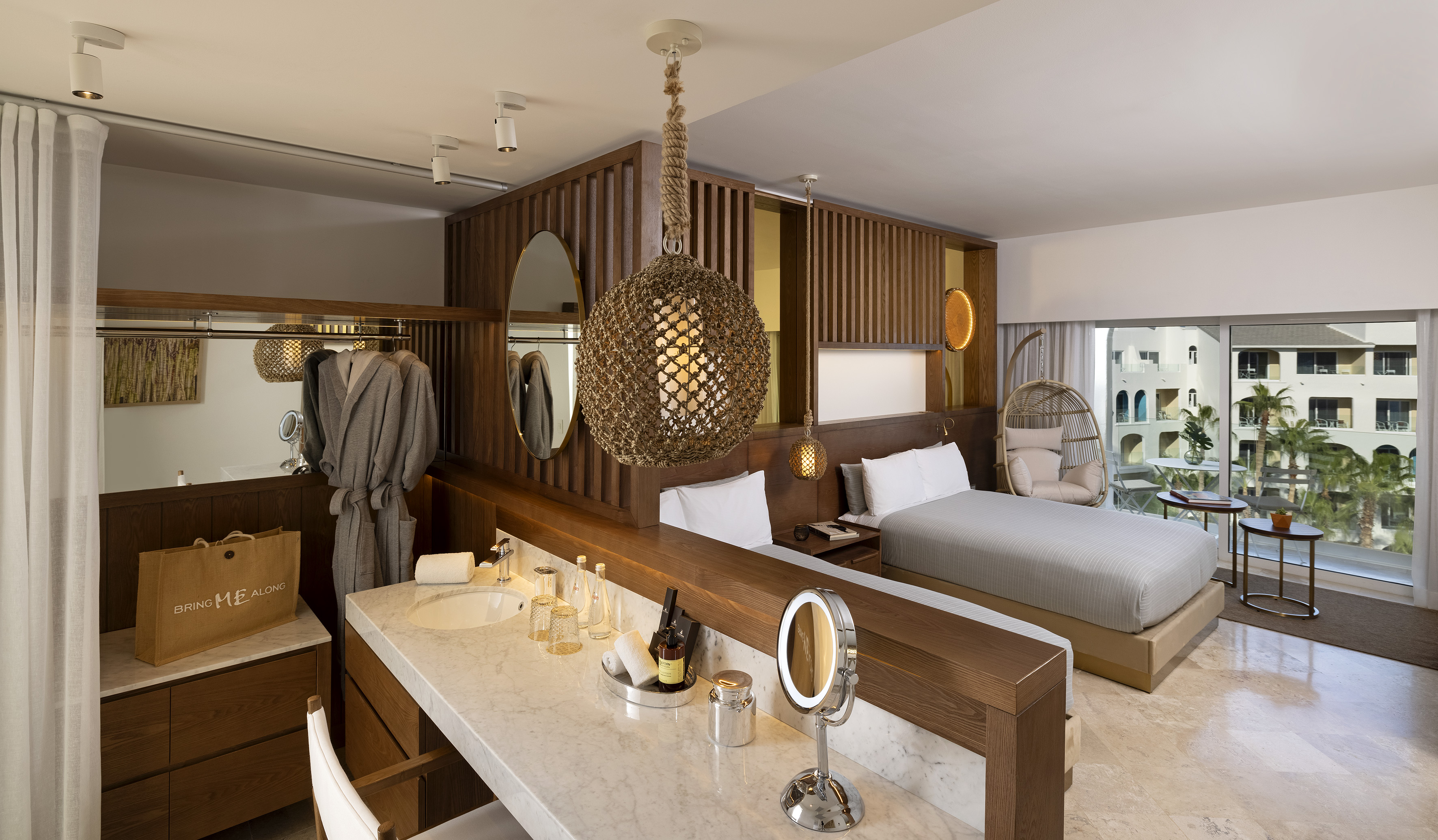 Modern hotel room with bed, marble vanity, rope pendant light, and resort view.