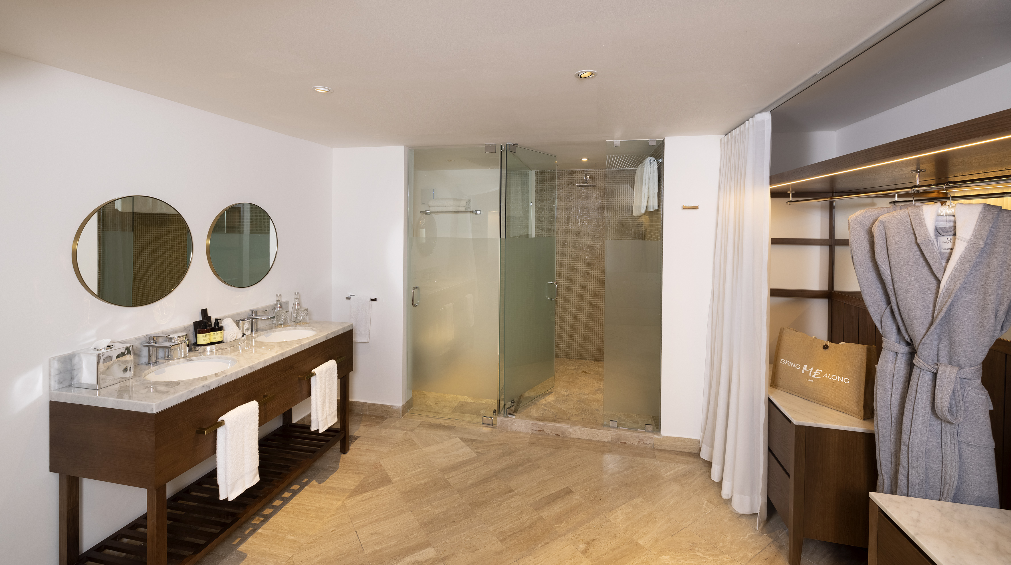 Modern bathroom with double vanity, glass shower, and hotel robe.