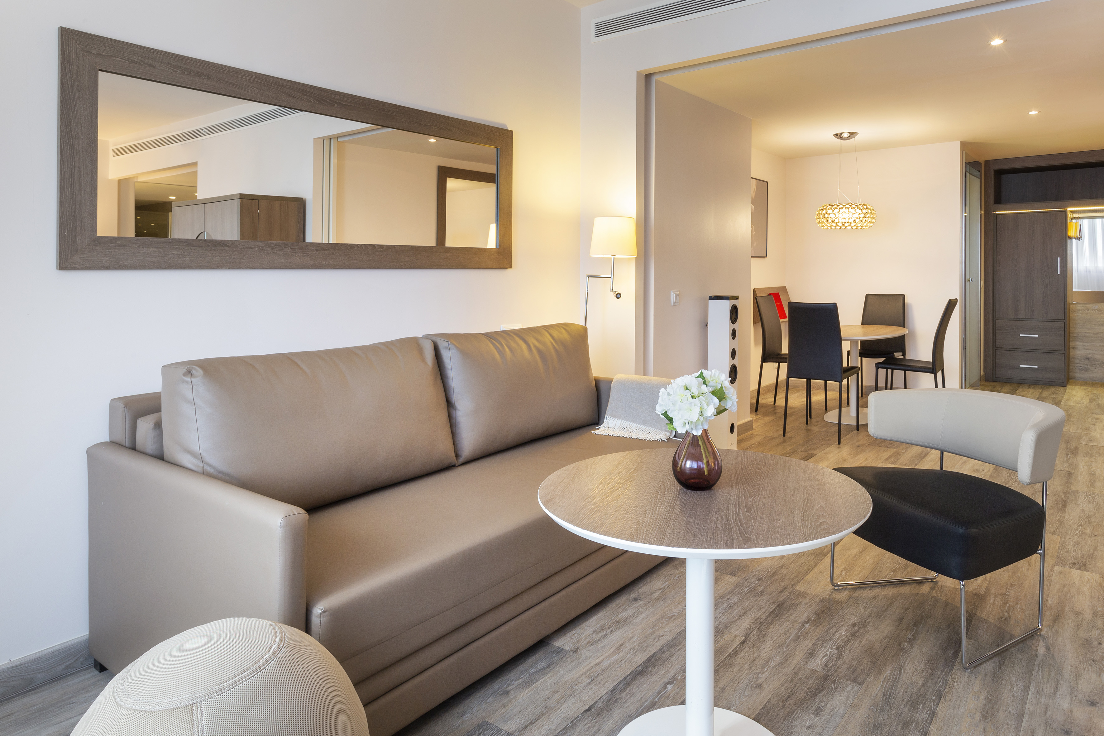 Modern apartment interior with tan sofa, large mirror, and dining area.