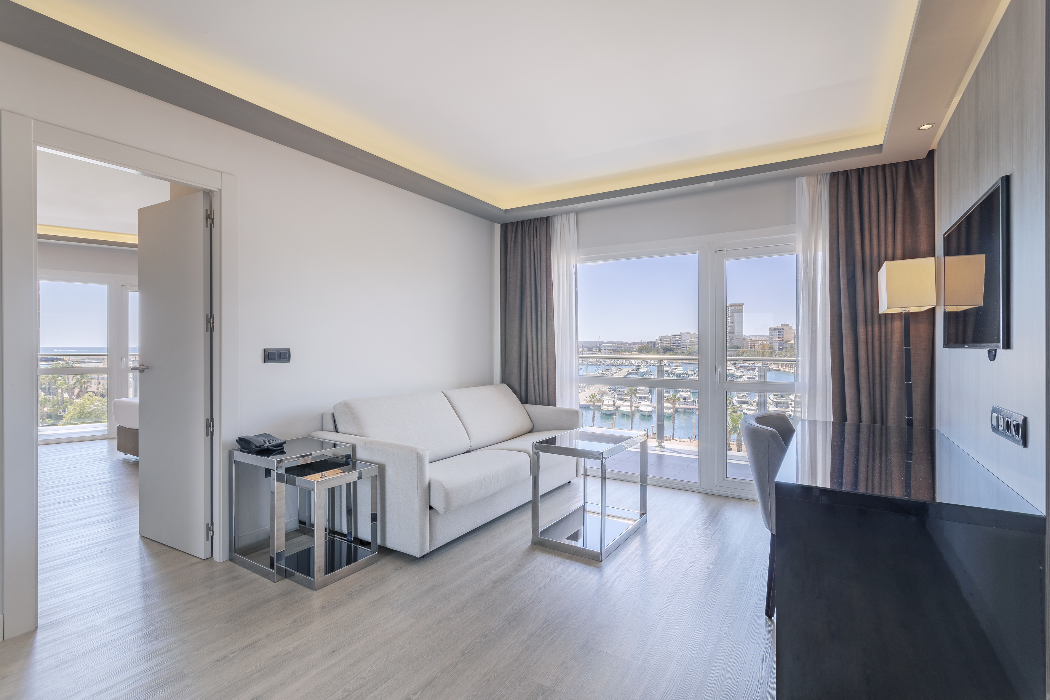 Modern hotel living room with white sofa and balcony overlooking marina.