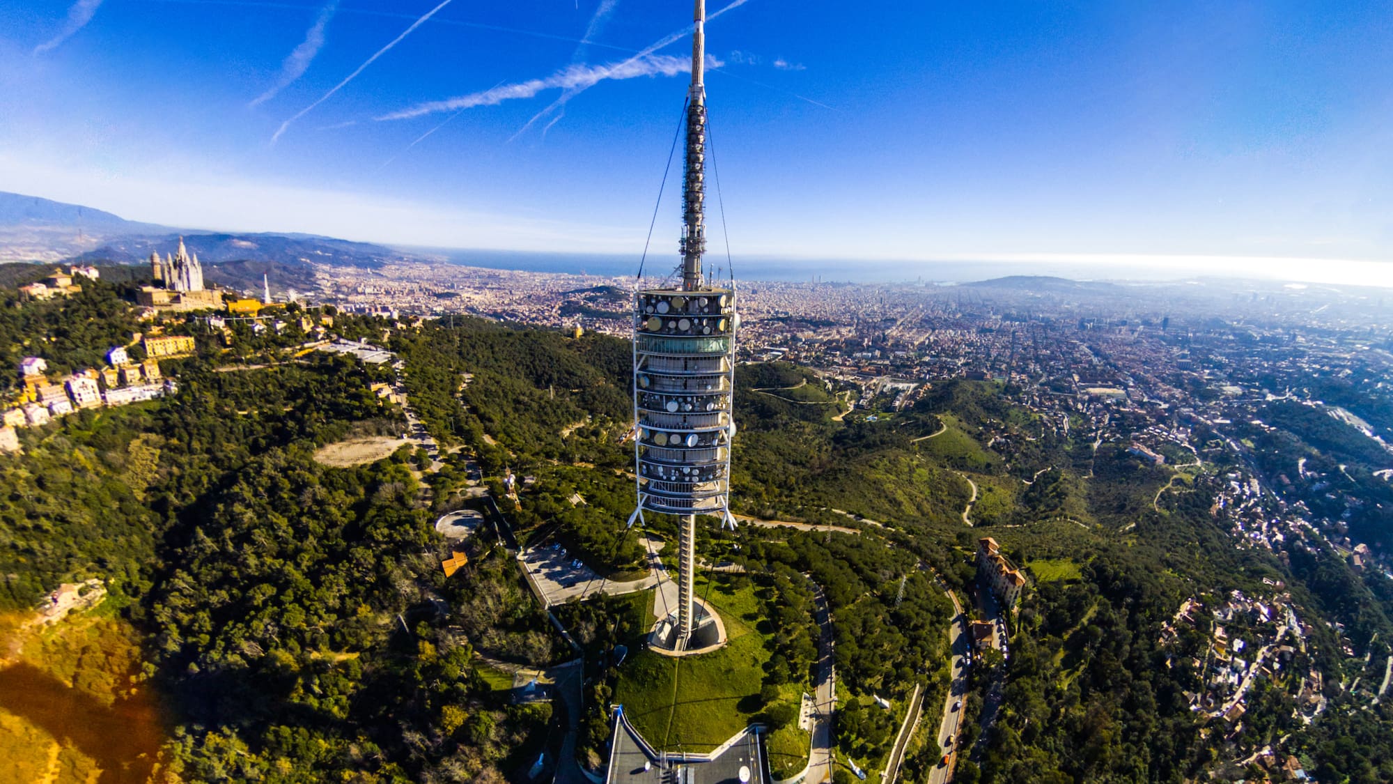 a tower on a hill with trees and a city in the background