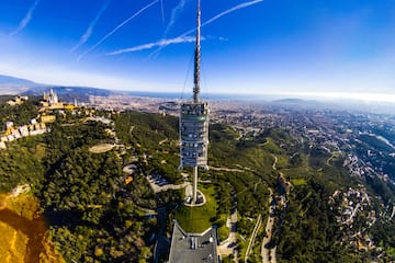 a tower on a hill with trees and a city in the background