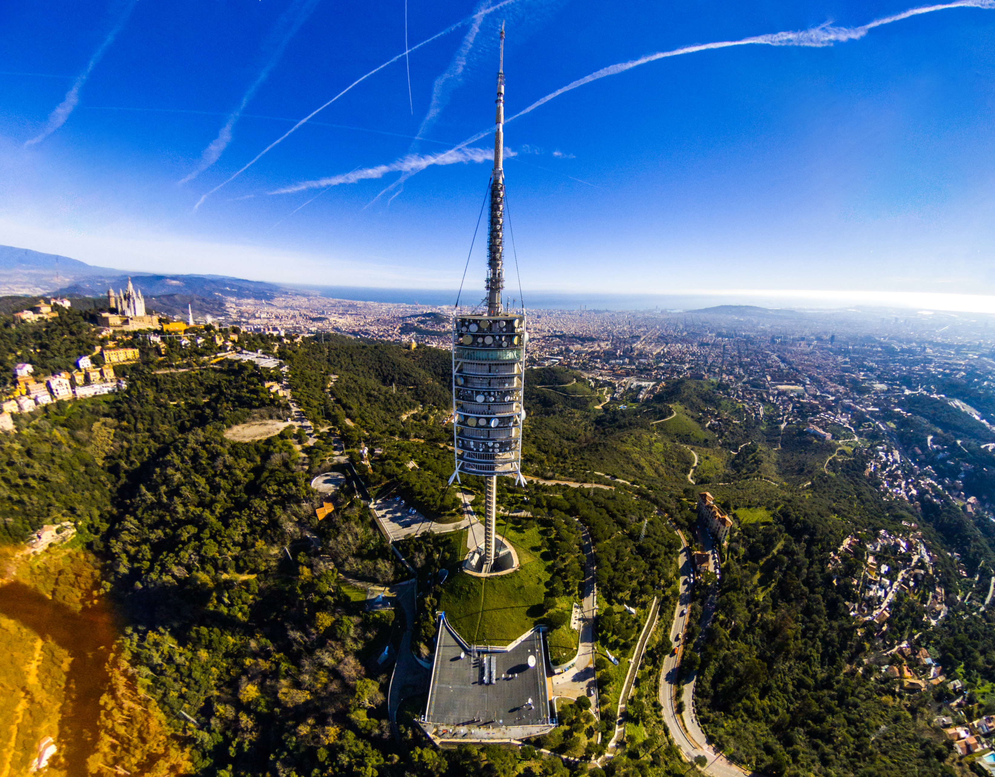 a tower on a hill with trees and a city in the background