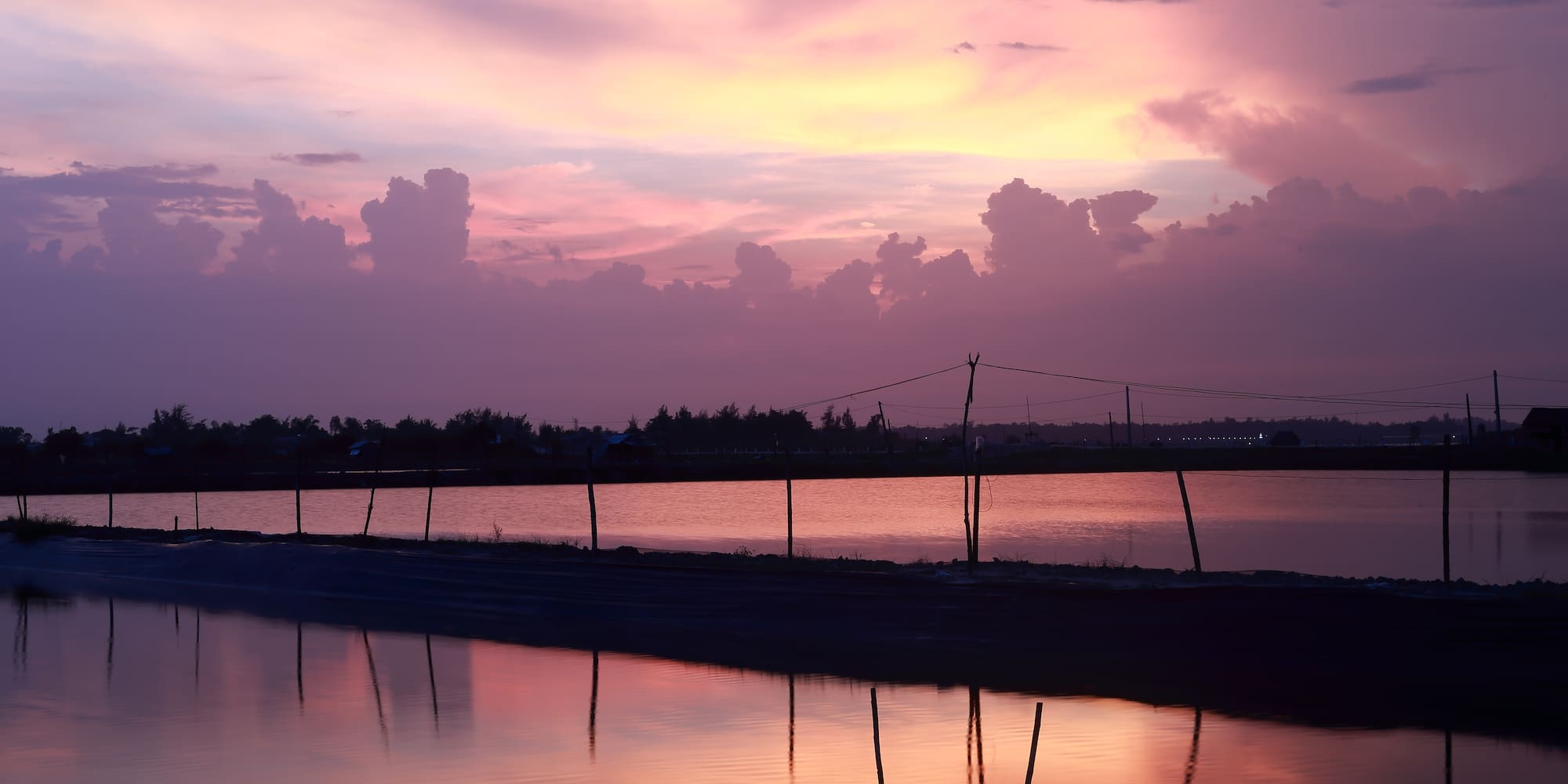 a body of water with a fence and trees in the background