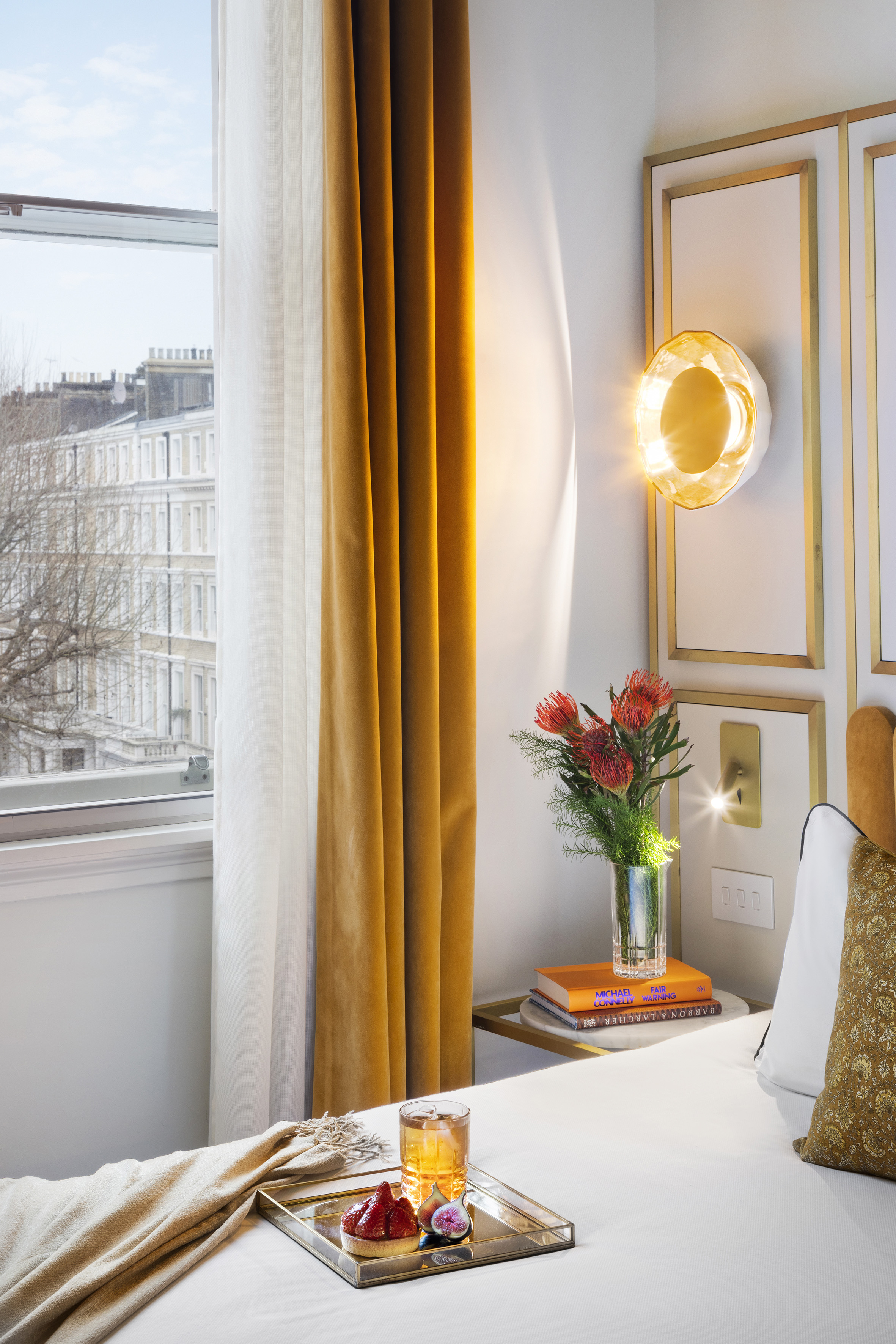 Golden curtains in a luxury hotel bedroom with city view and dessert tray.
