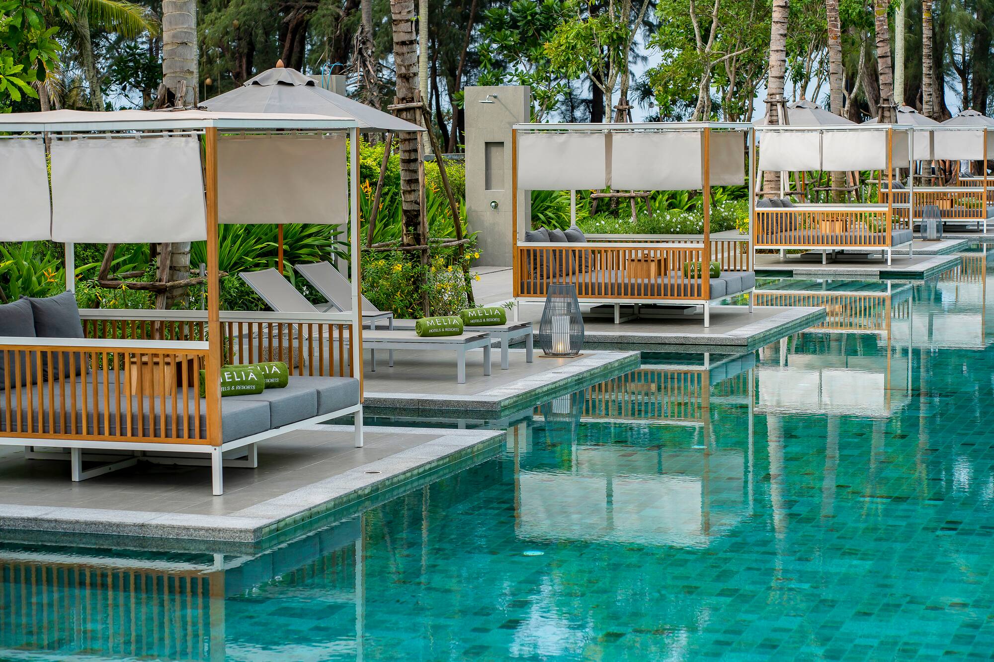 Row of poolside cabanas with gray cushions and Melia towels at a tropical resort.