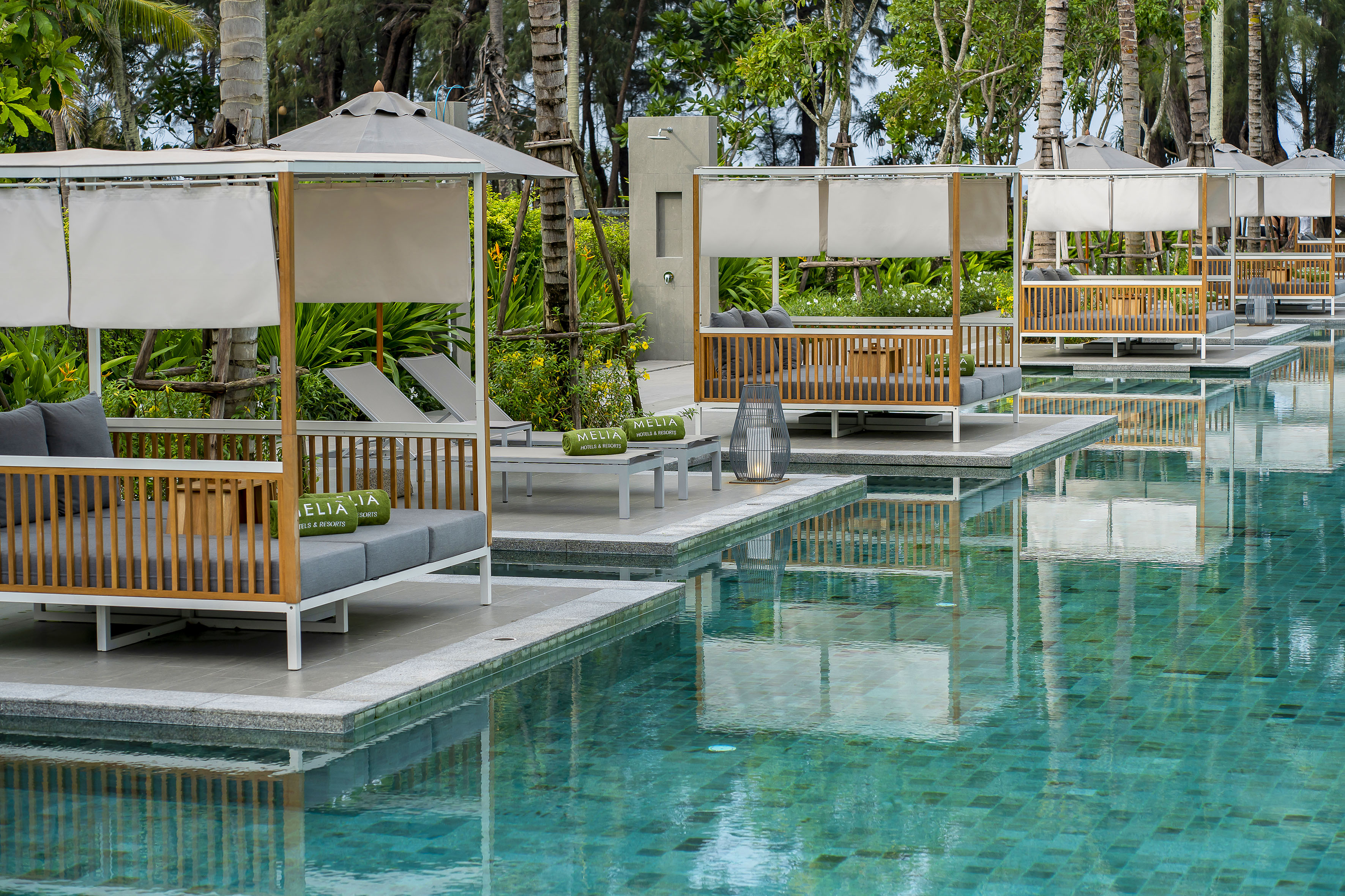 Row of poolside cabanas with gray cushions and Melia towels at a tropical resort.