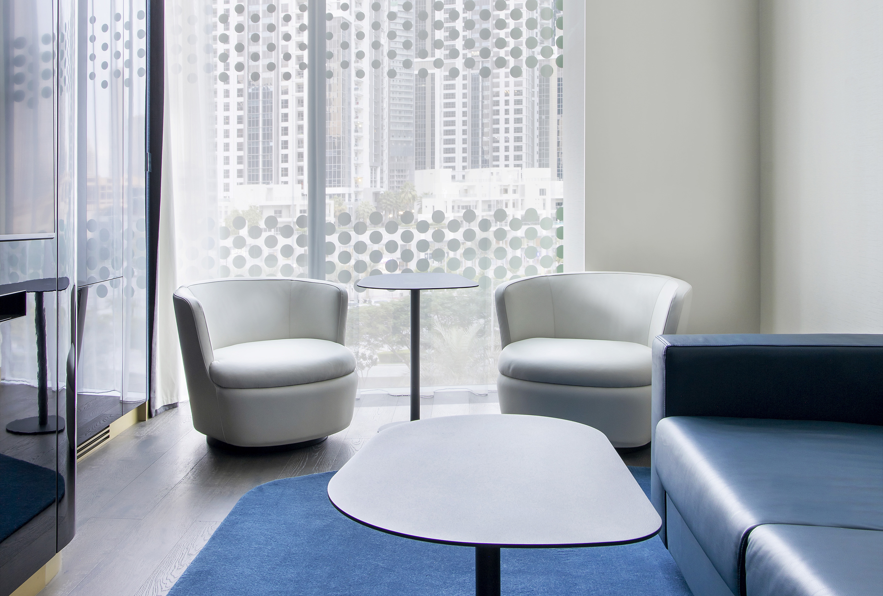 Contemporary lounge with white armchairs, blue sofa, and city view.
