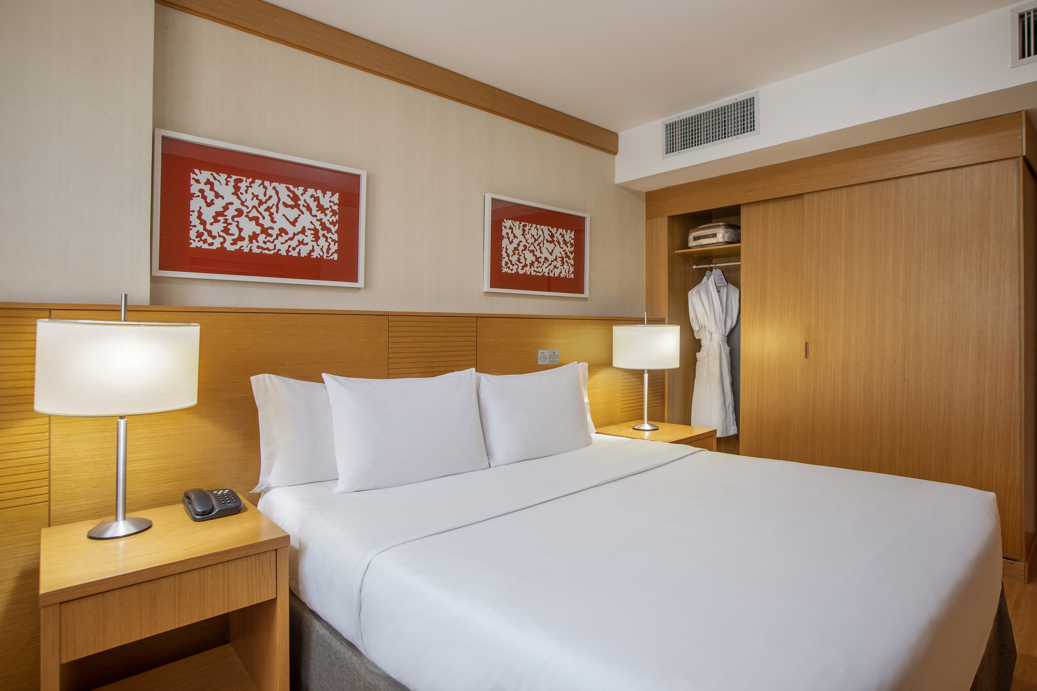 Cozy hotel bedroom with white bed, wood accents, bedside lamps, and modern art.