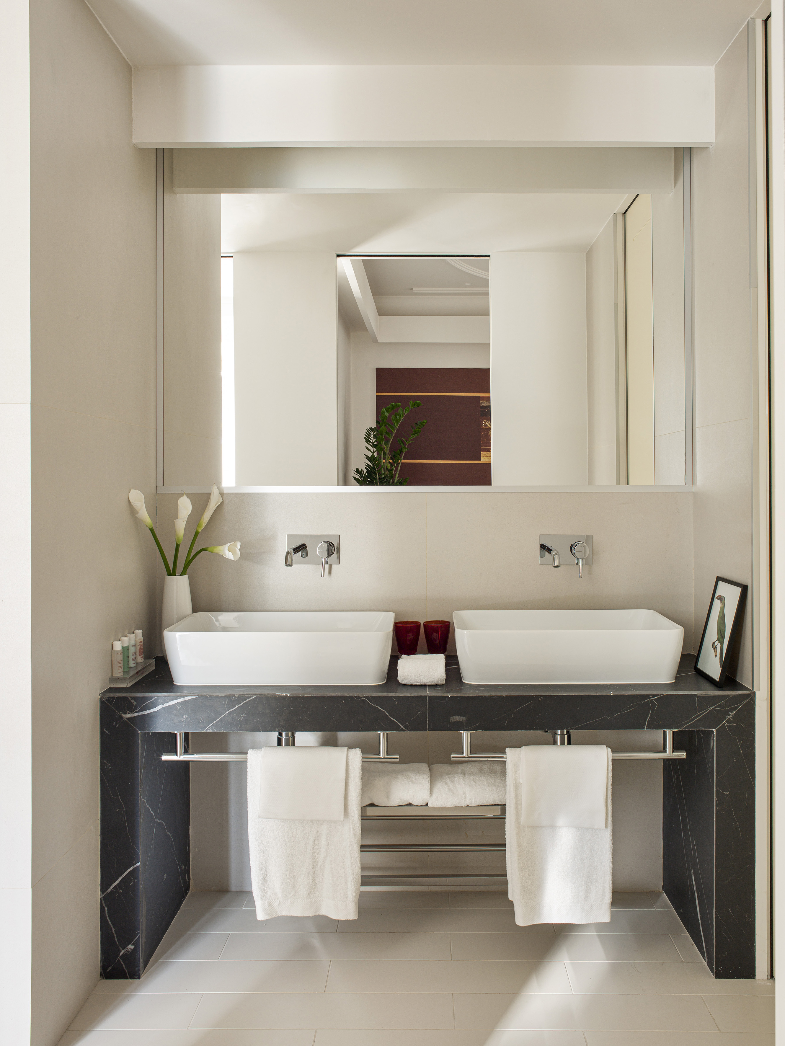 Black marble double sink vanity, white basins, large mirror, and white towels.