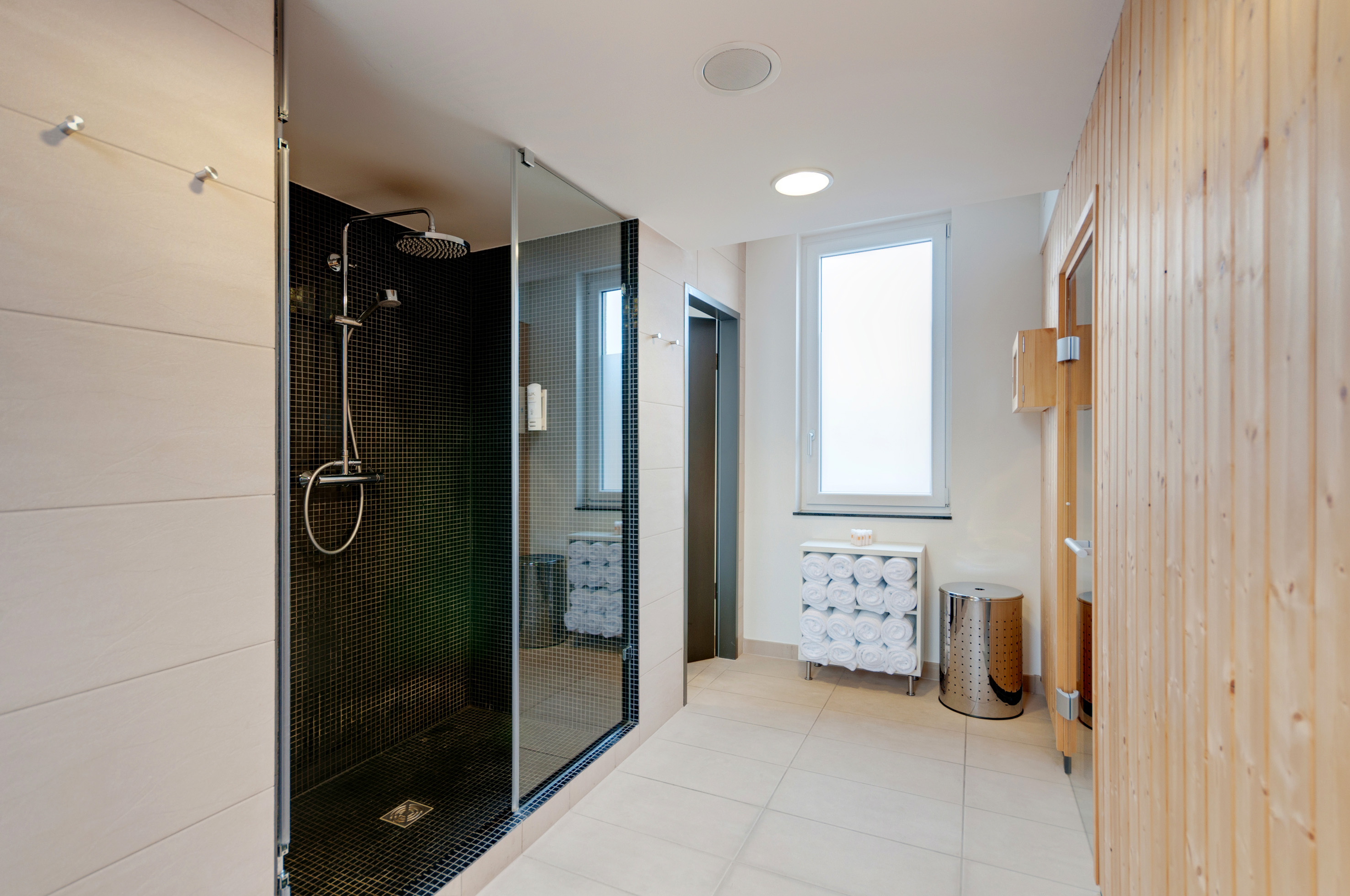 Modern spa bathroom with glass shower, black tiles, rolled towels, wood wall.