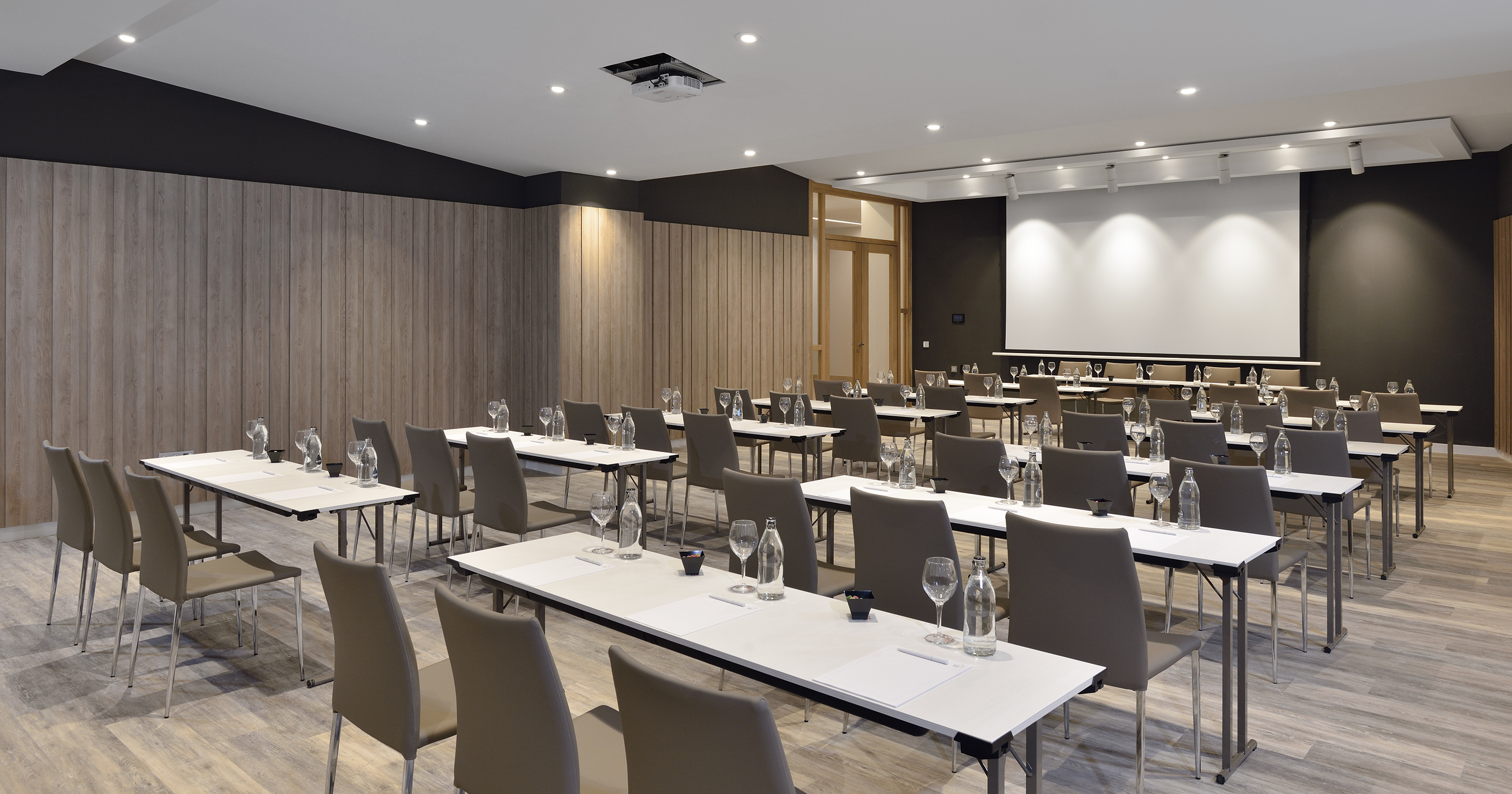 Empty modern conference room with tables, chairs, and large projector screen.