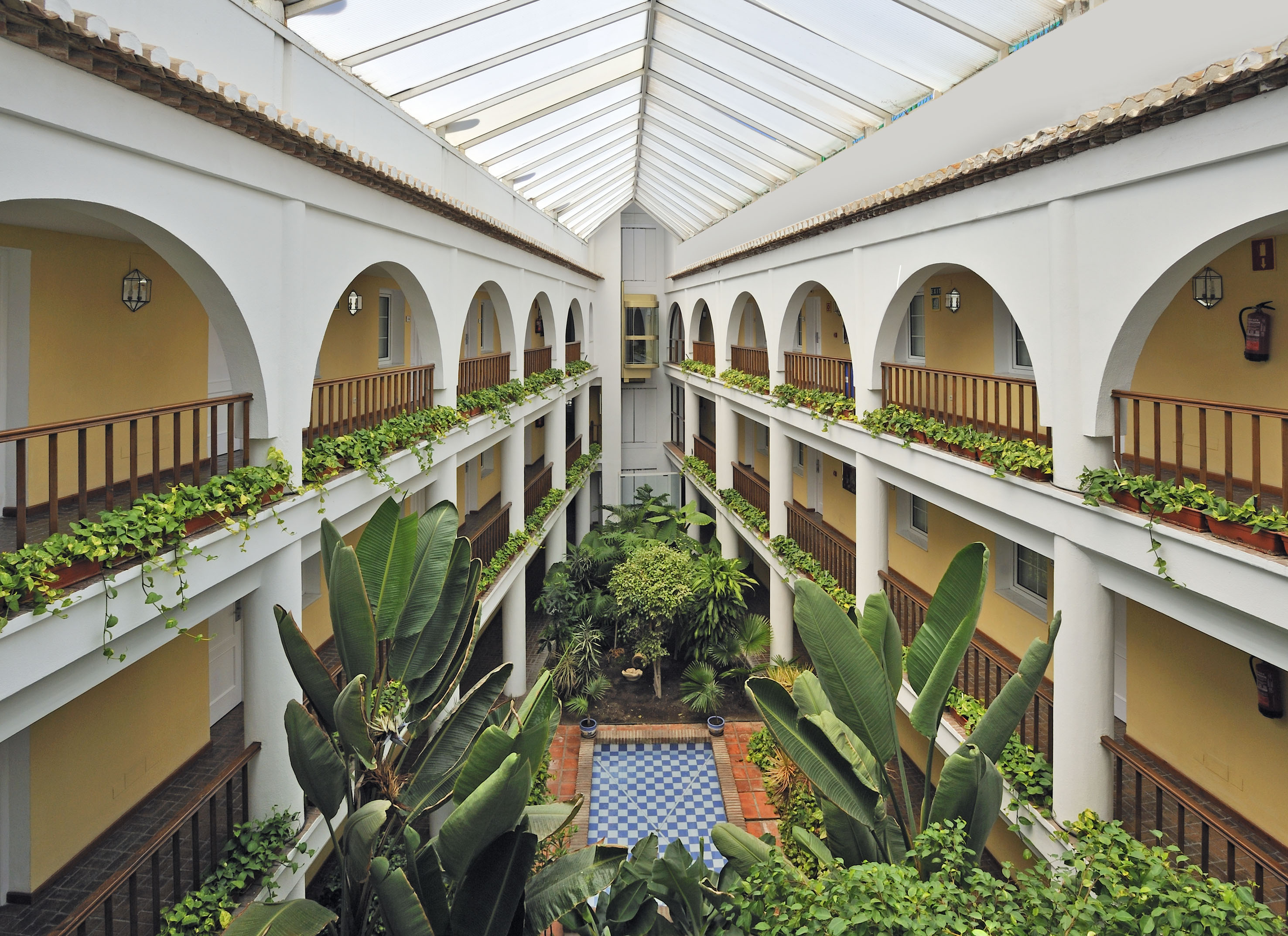 Lush tropical hotel atrium with arched balconies, glass roof, and tiled garden pool.