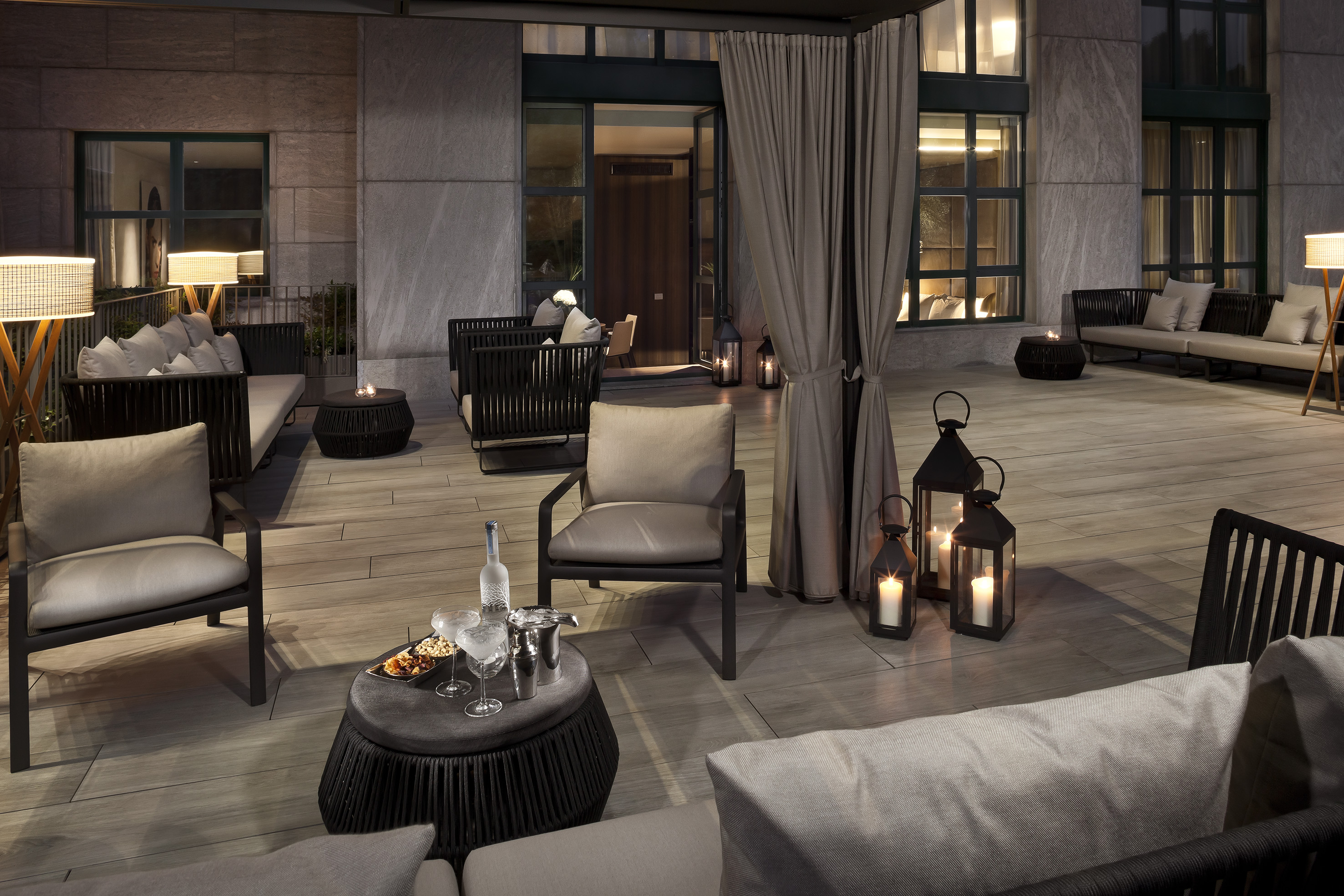 Luxury outdoor patio at night with modern furniture, lanterns, and drinks.